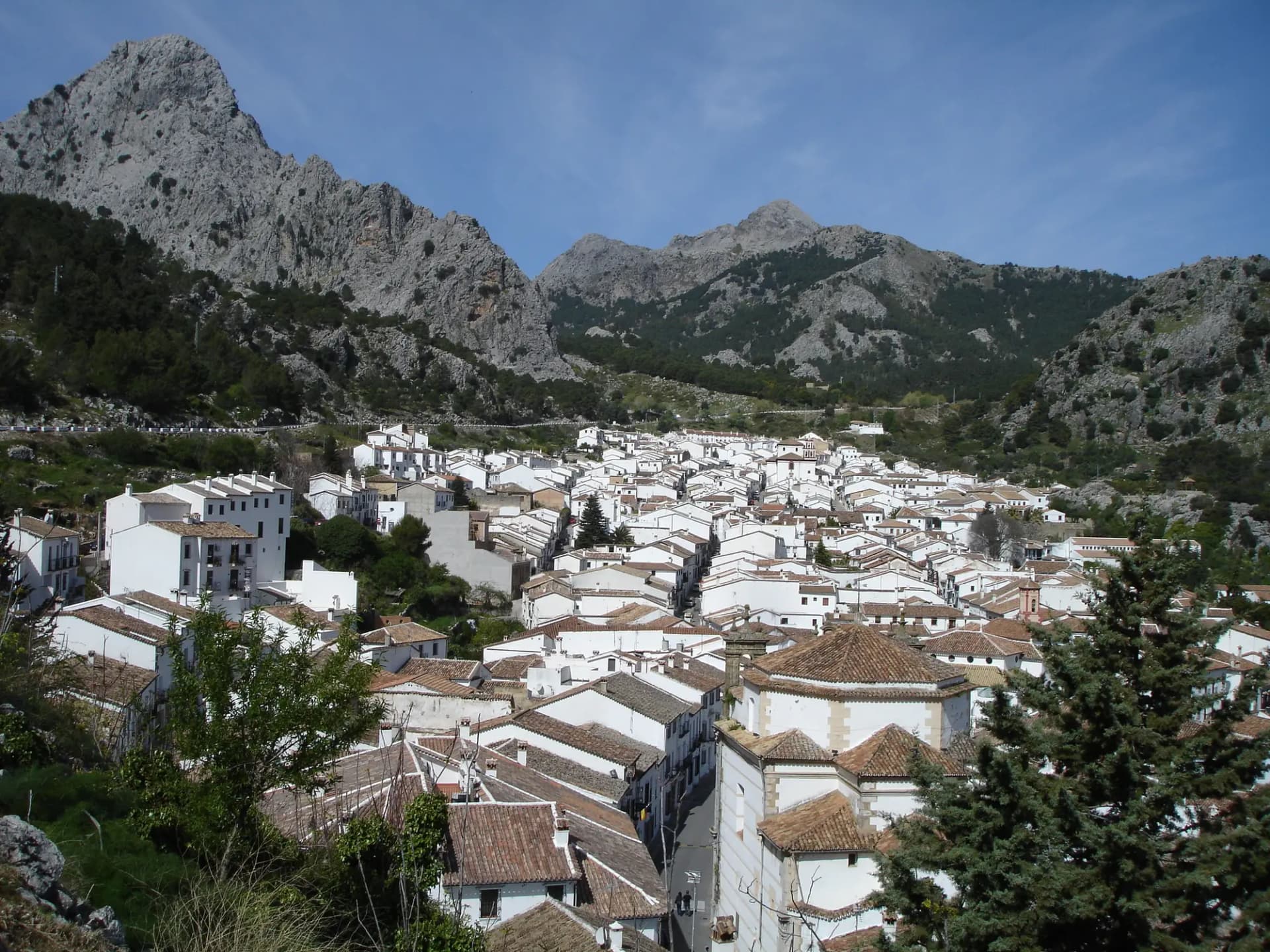 Tejados de teja y casas blancas de Grazalema bajo un cielo azul y una sierra de roca caliza al fondo