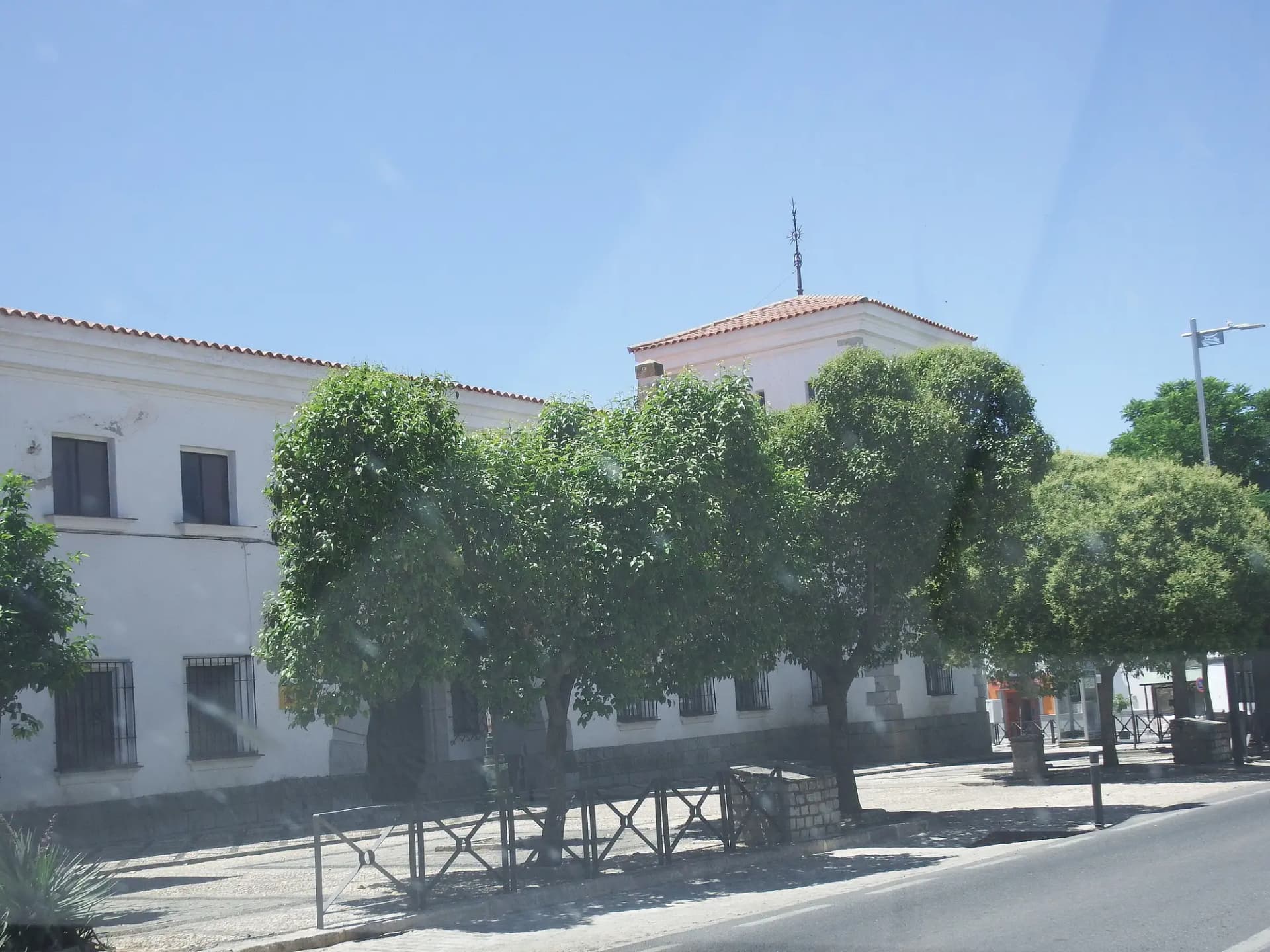 Edificio blanco con torre y árboles en una calle céntrica de Alcaracejos