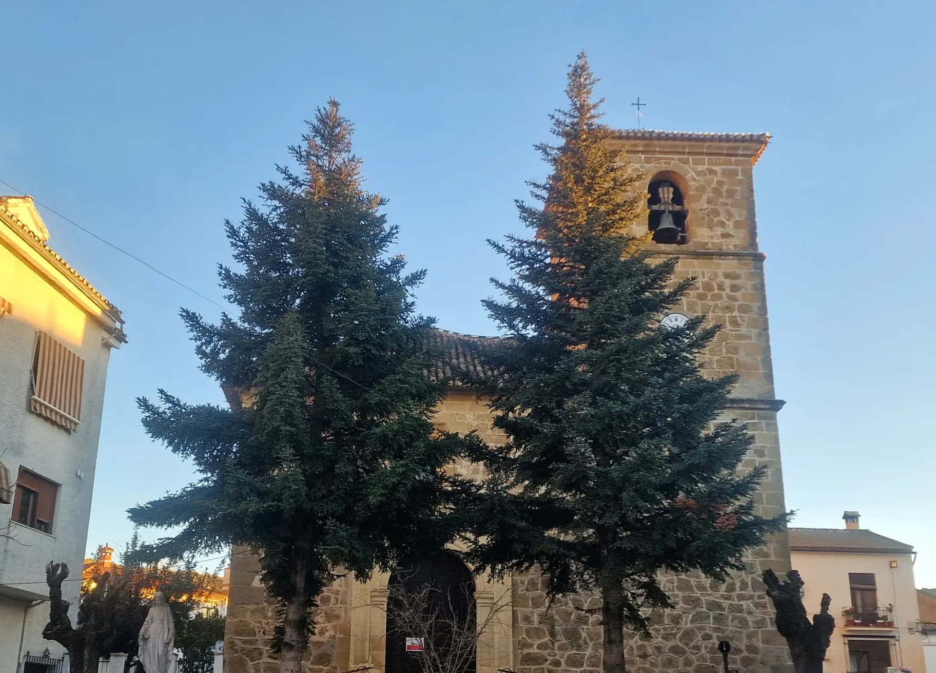 Torre de piedra de la iglesia de la Inmaculada Concepción de Beas de Granada entre dos abetos