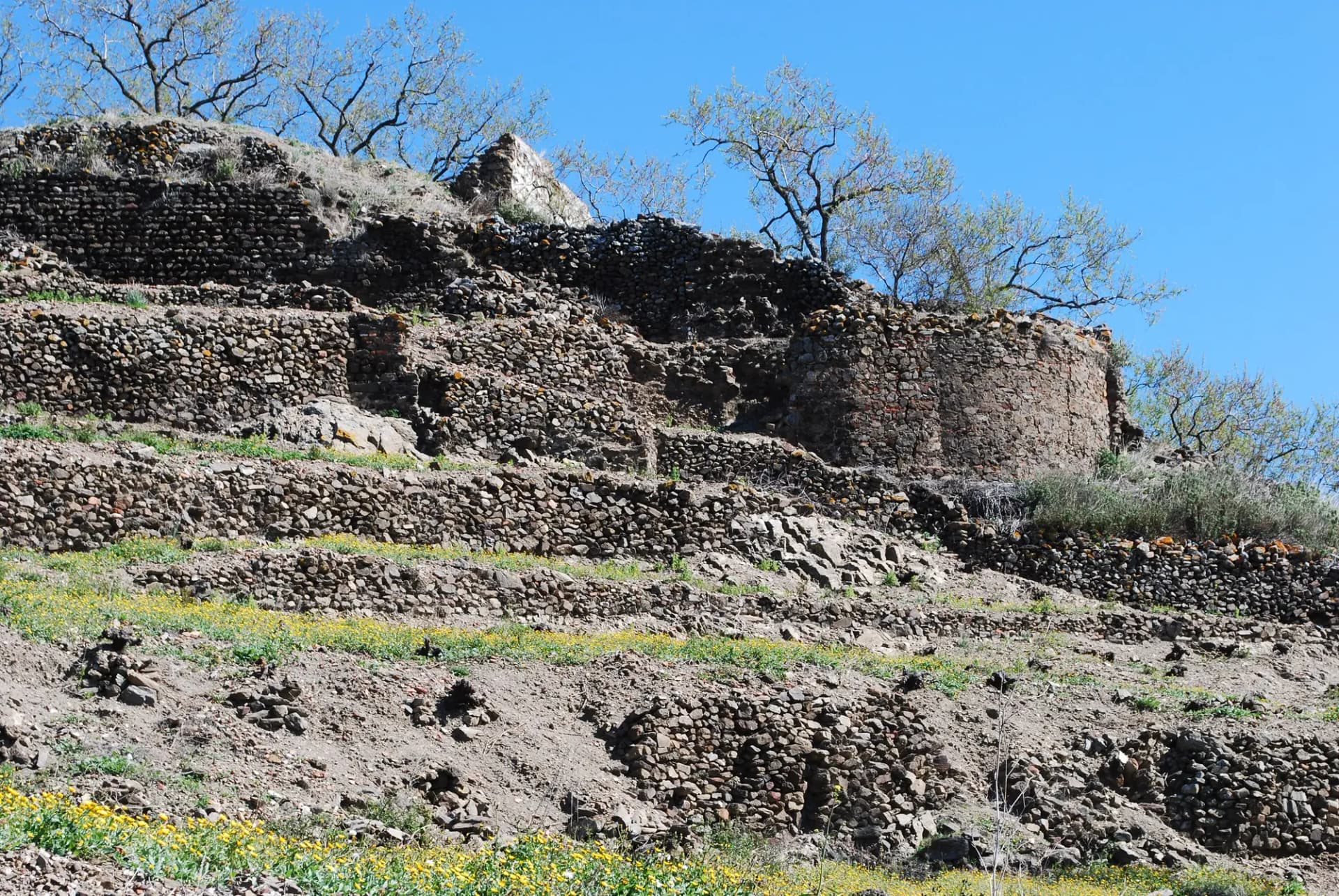 Muros y terrazas de piedra del castillo de Bentomiz sobre un cerro verde