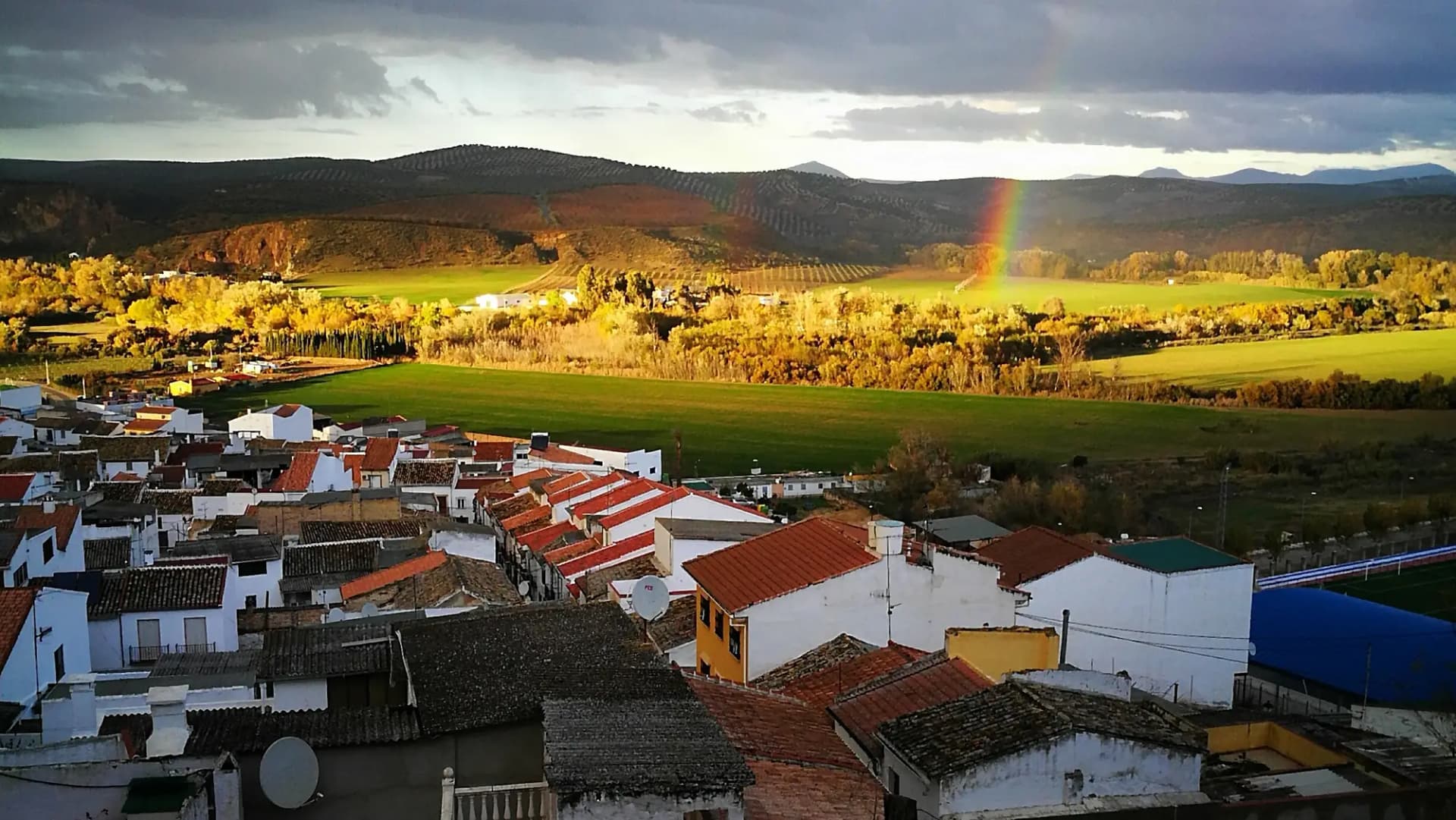 Tejados y casas de Cuevas Bajas con la campiña verde y un arcoíris al fondo