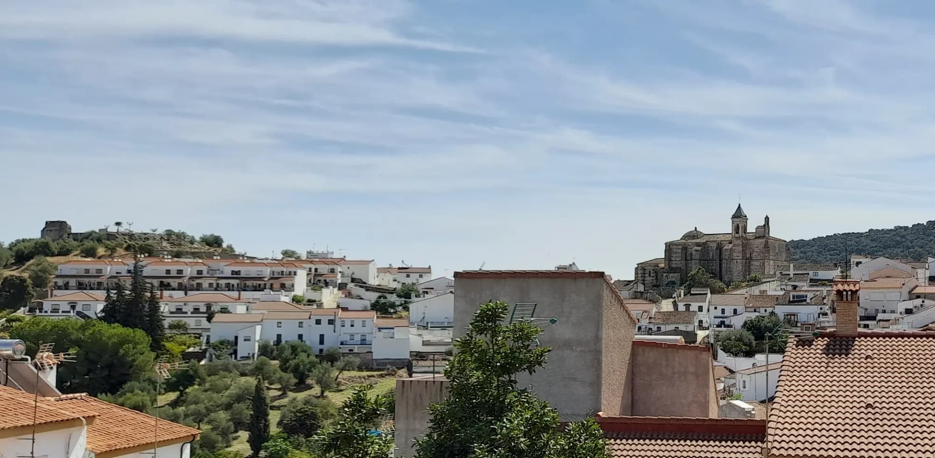 Casas y tejados de El Castillo de las Guardas con la iglesia de San Juan Bautista al fondo bajo un cielo con nubes