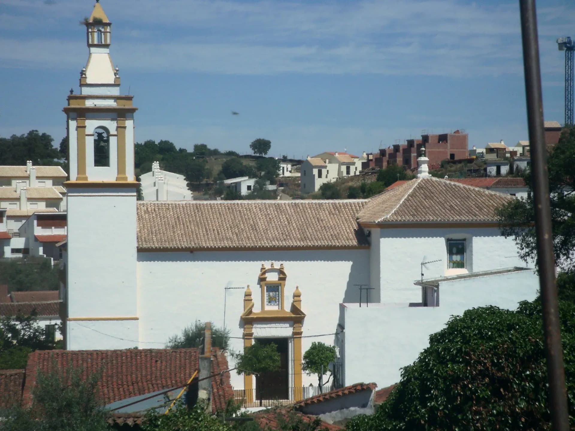 Parroquia del Divino Salvador de El Ronquillo, con su torre blanca, y casas del pueblo al fondo