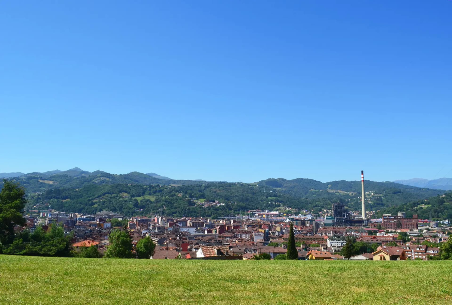 Vista de La Felguera, en Langreo, con una chimenea industrial y los montes del valle del Nalón al fondo