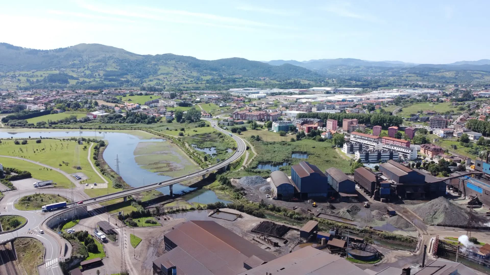 Vista aérea de la ría de Boo a su paso por Maliaño, con naves industriales y los montes del valle de Camargo al fondo