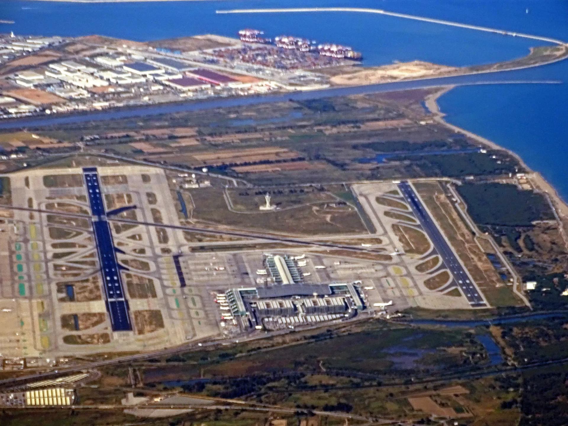 Vista aérea del aeropuerto del Prat con sus pistas, el delta del Llobregat y el puerto de Barcelona al fondo