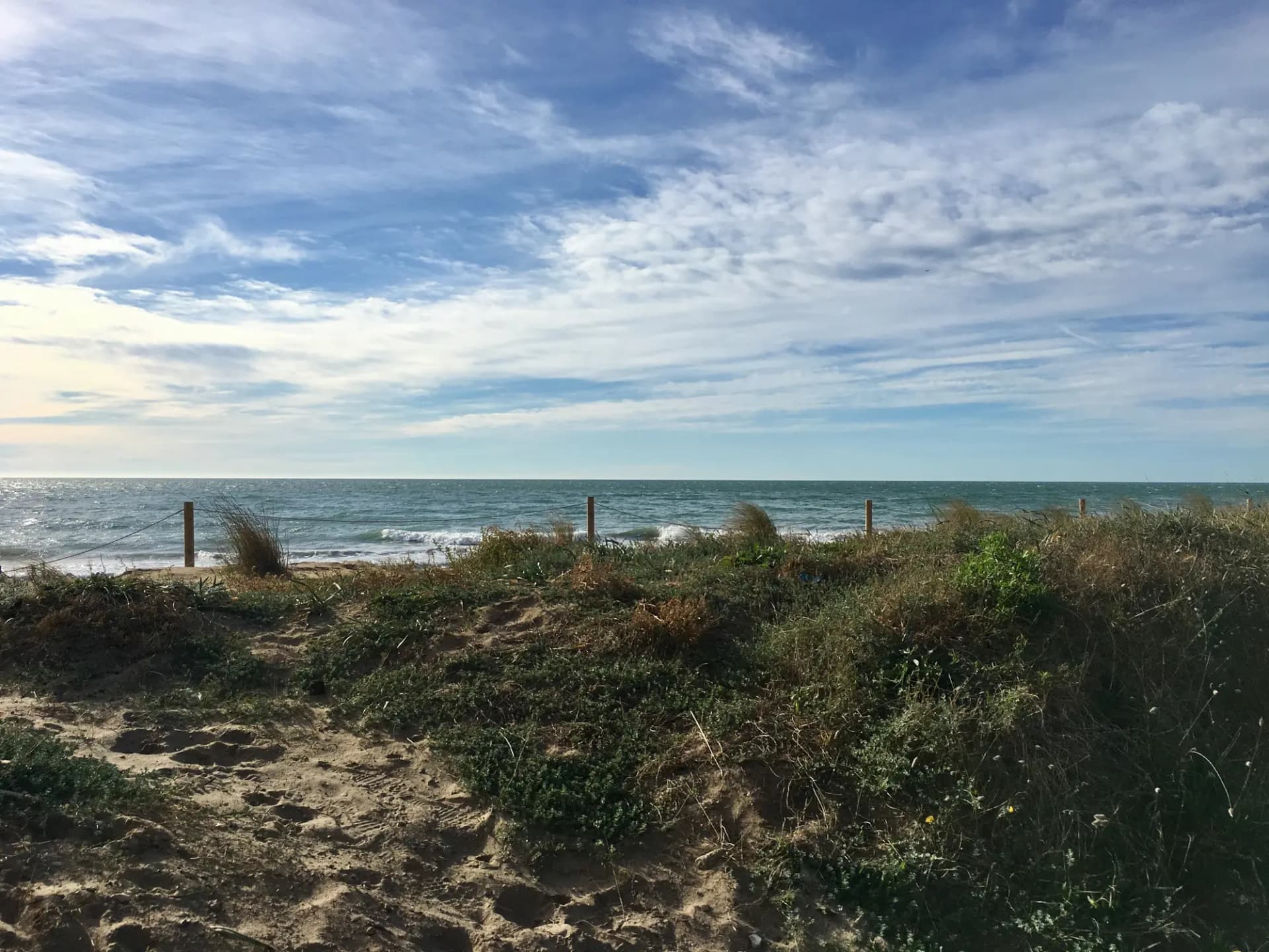 Dunas con vegetación y la playa de Gavà frente al mar bajo un cielo con nubes