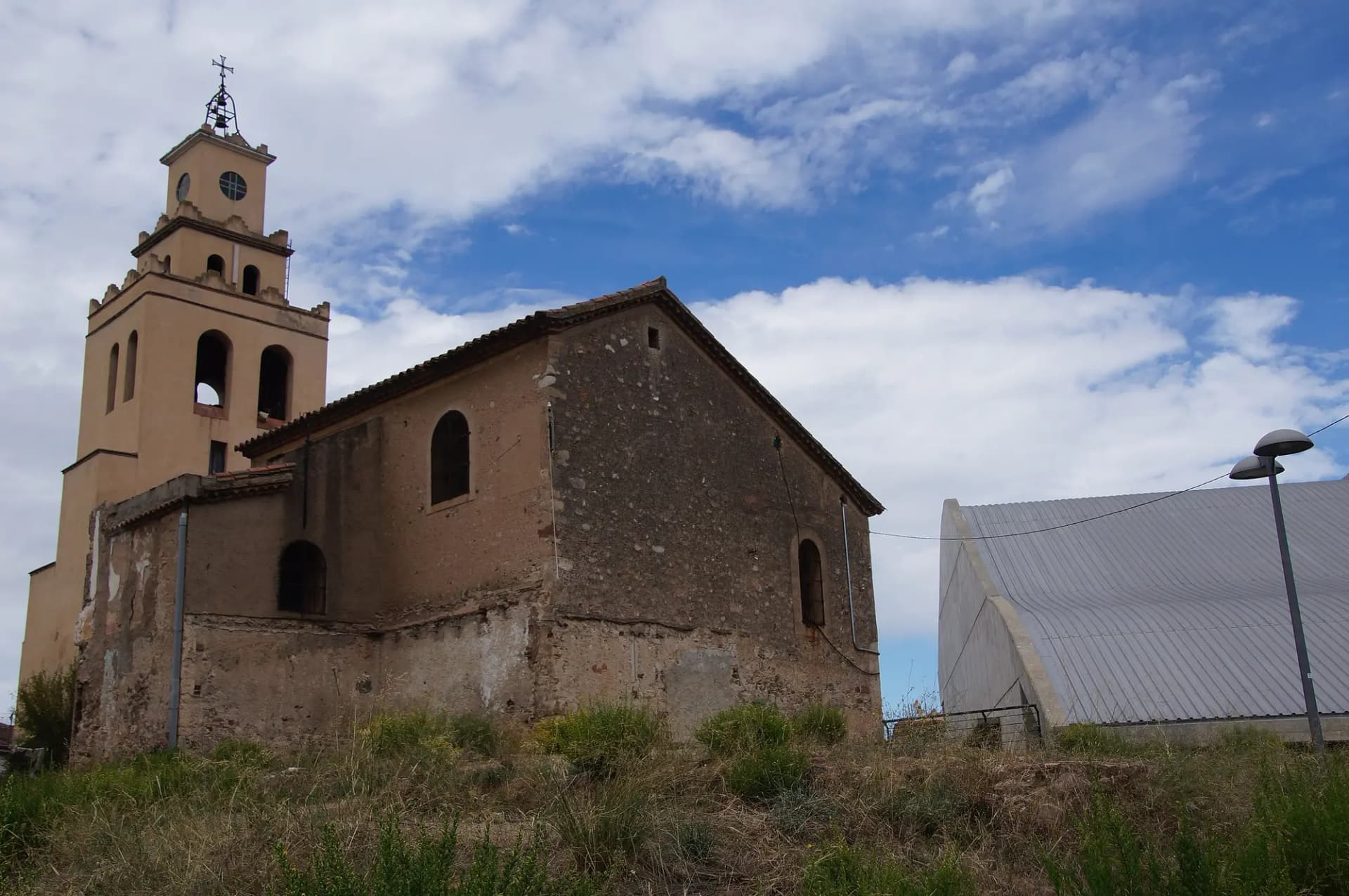 Iglesia parroquial de Sant Quirze del Vallès, de piedra, con campanario y cielo con nubes