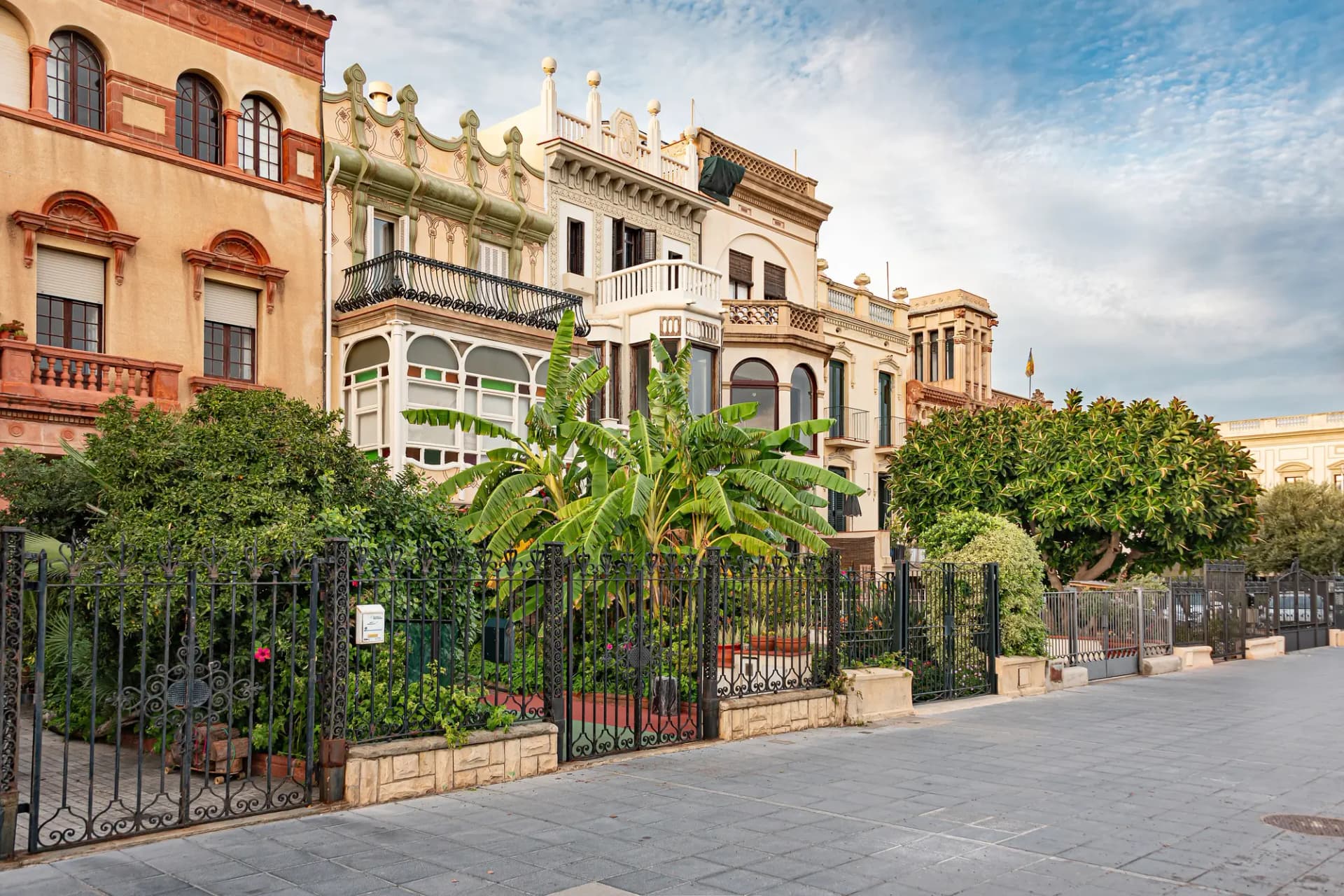 Casas modernistas con balcones y jardines en una calle de Vilassar de Mar bajo un cielo azul