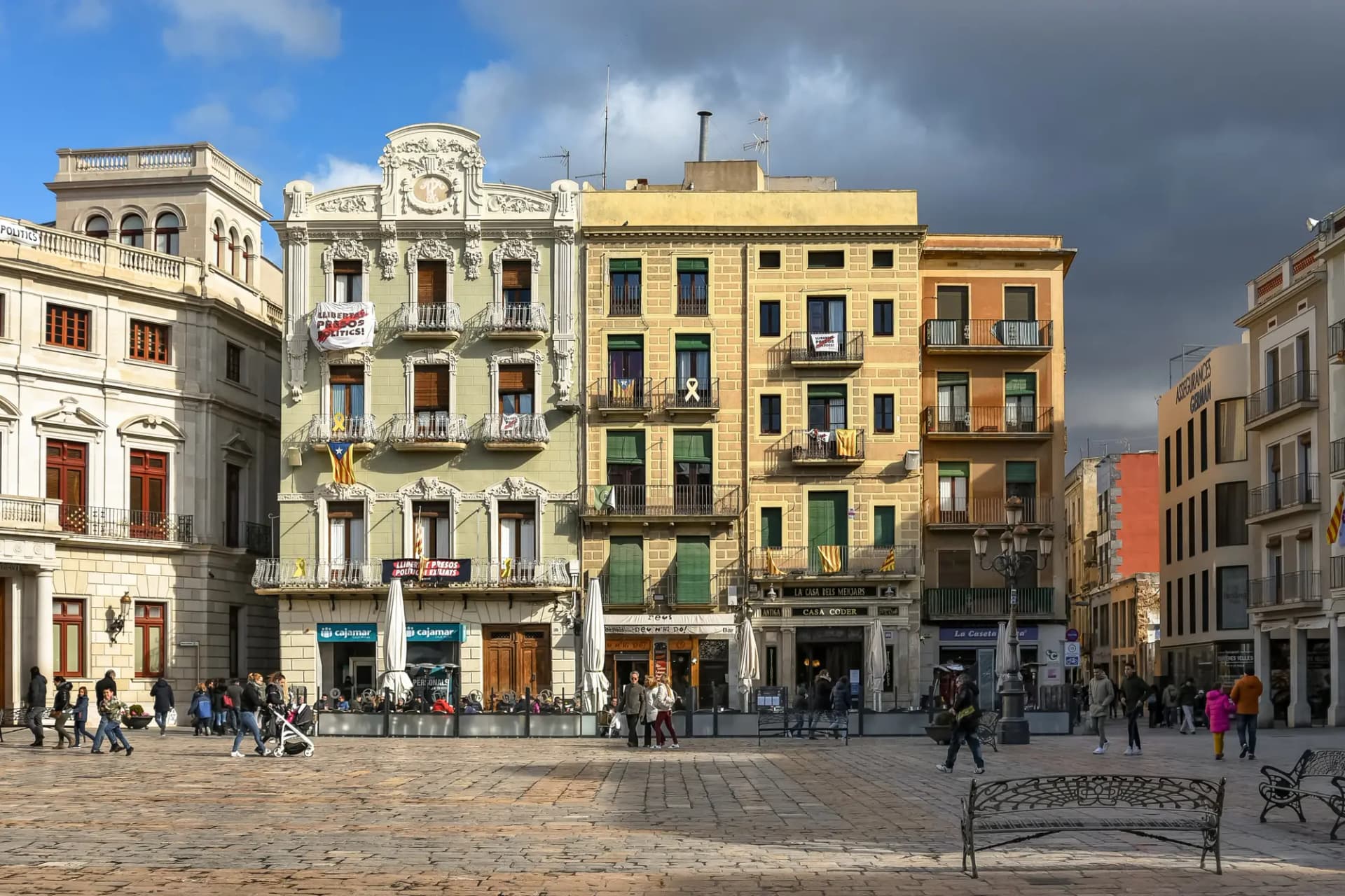 Plaça del Mercadal de Reus con fachadas modernistas de colores y gente paseando bajo un cielo nublado