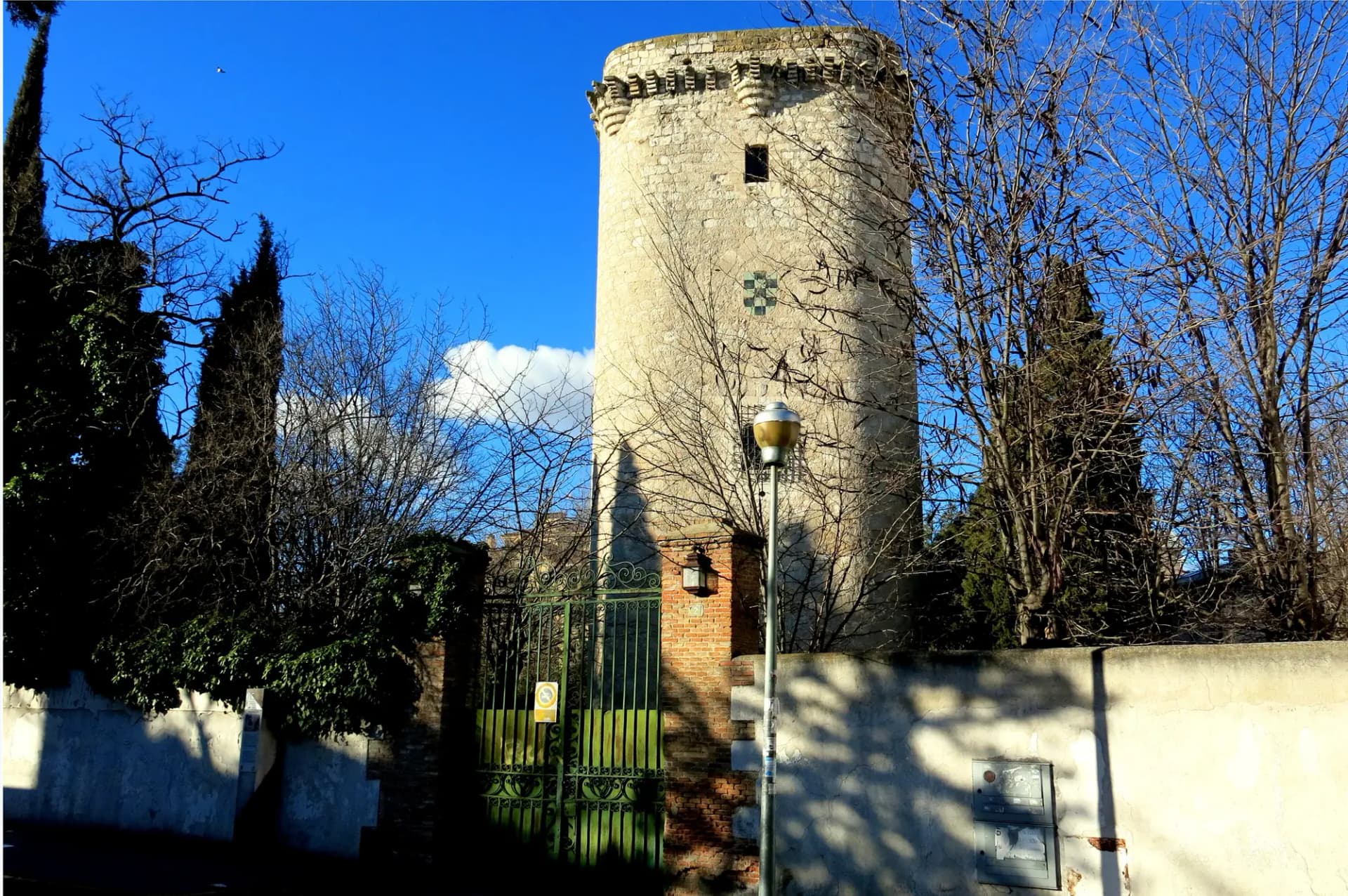 Torre de Éboli de Pinto, de piedra, entre cipreses y árboles bajo un cielo azul