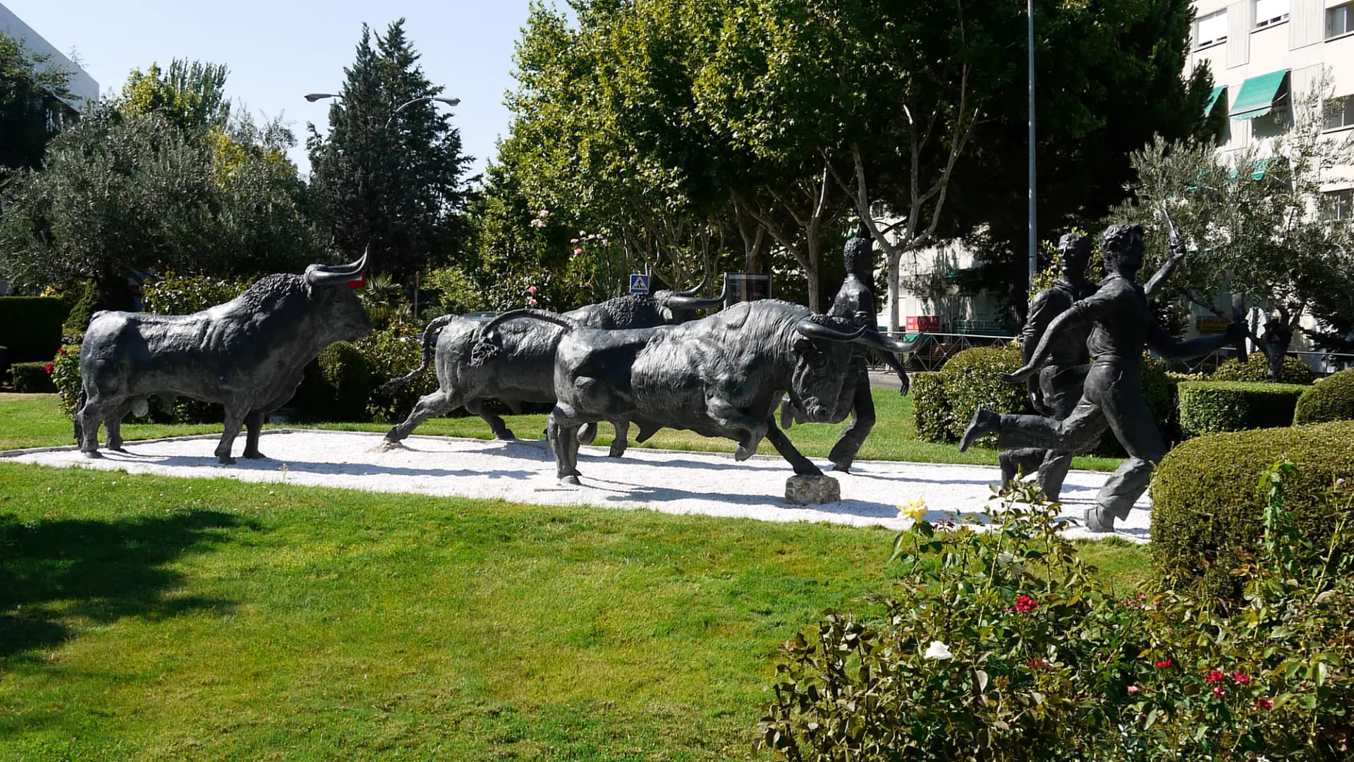 Esculturas de bronce de toros y corredores en una rotonda ajardinada