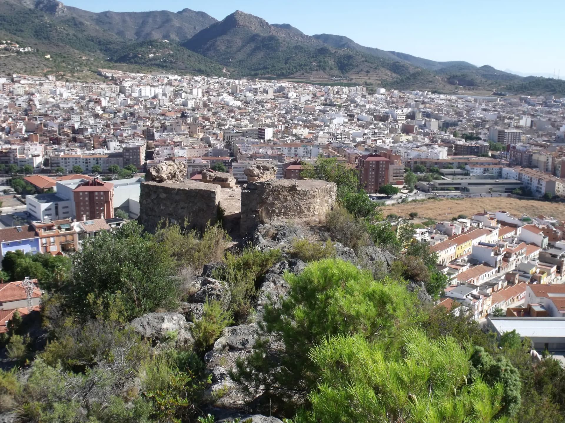 Vista de La Vall d'Uixó desde un cerro con restos de muralla, con la ciudad y las montañas al fondo