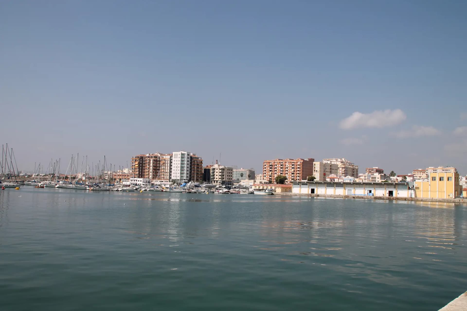 Puerto de Vinaròs con el agua en calma y los edificios del frente marítimo al fondo