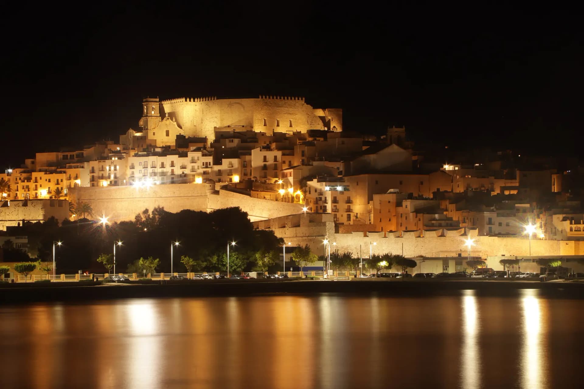 El castillo y el casco antiguo de Peñíscola iluminados de noche y reflejados en el agua