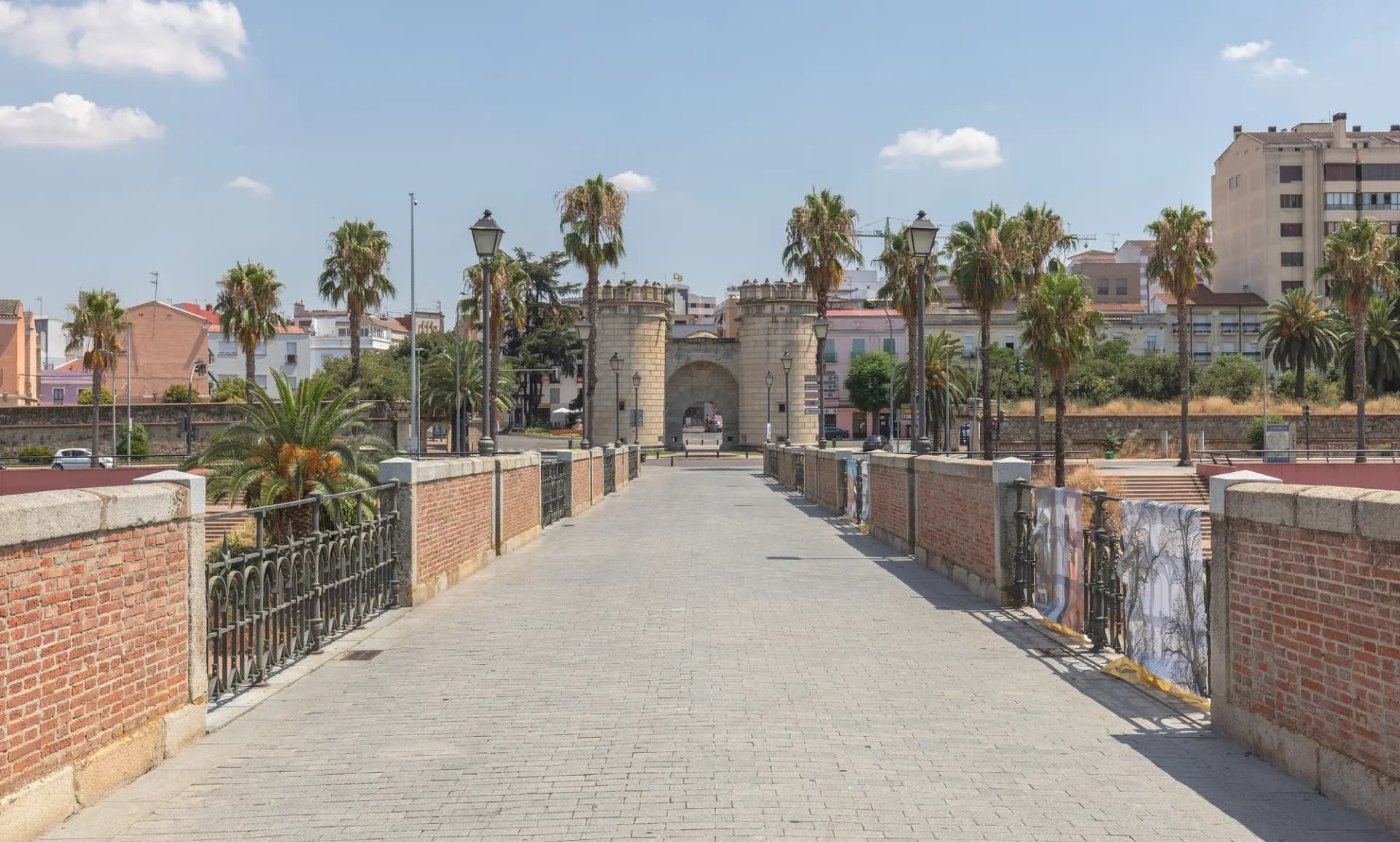 Calzada del Puente de Palmas de Badajoz, con palmeras a los lados y la Puerta de Palmas al fondo