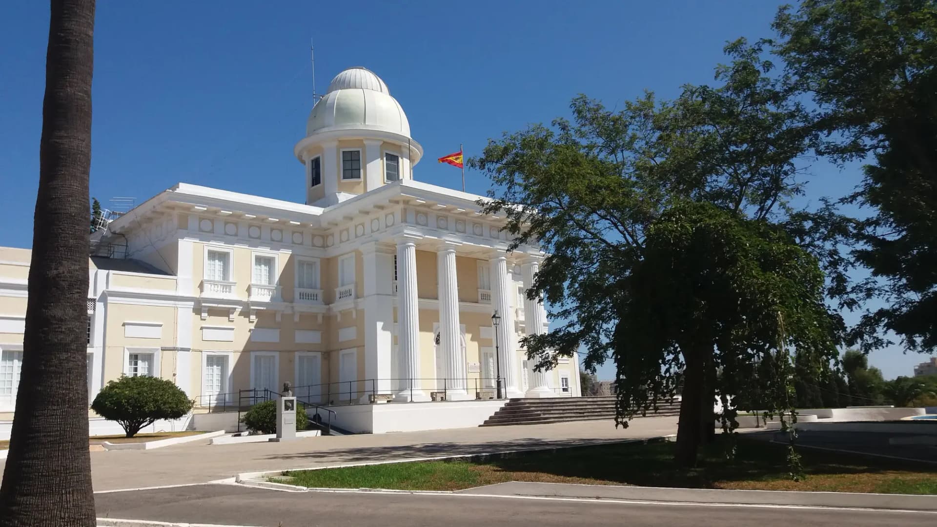 Edificio neoclásico blanco del Real Observatorio de la Armada con su cúpula, entre palmeras
