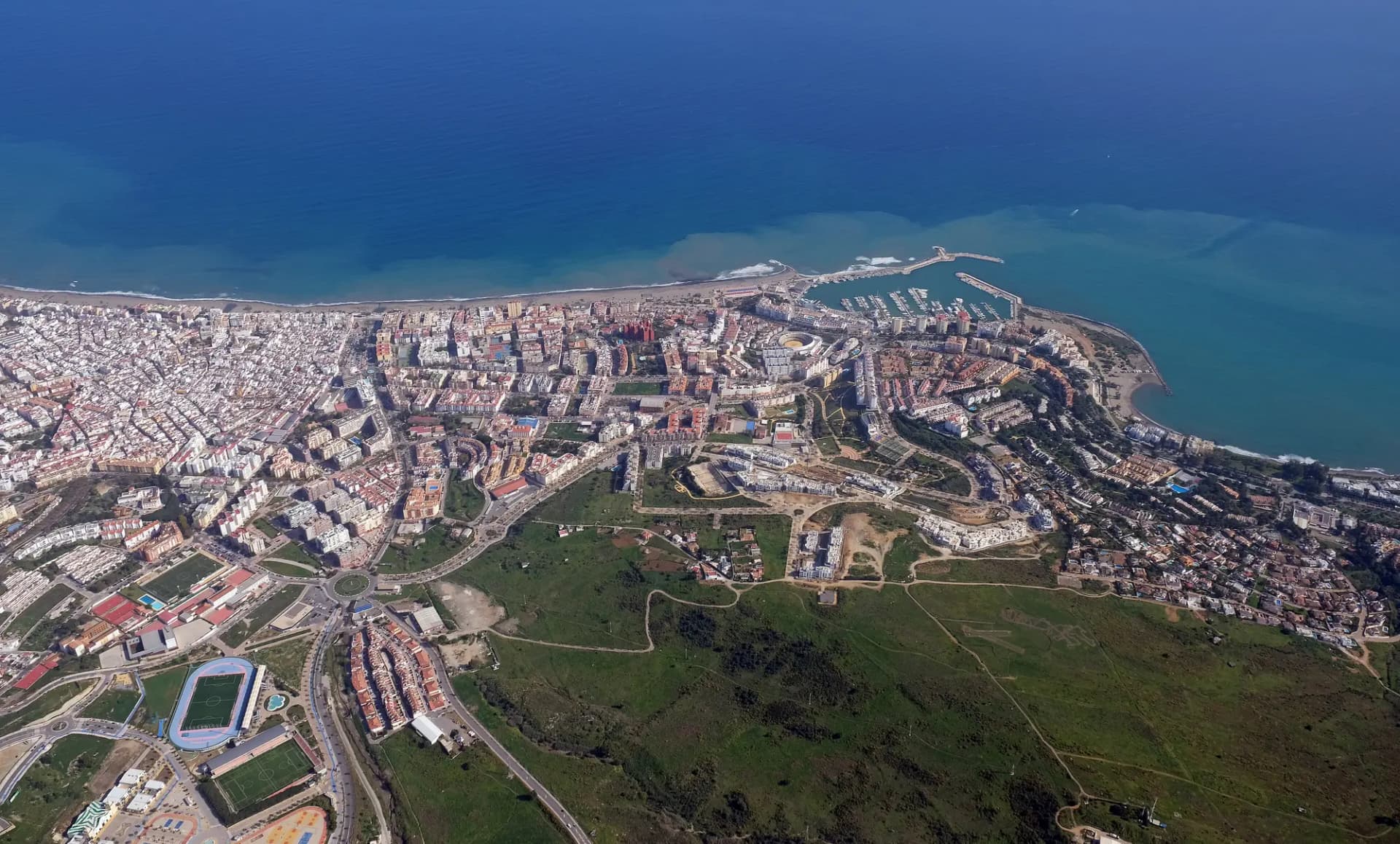 Vista aérea de Estepona con la ciudad, el puerto deportivo y el campo verde entre la costa y la sierra