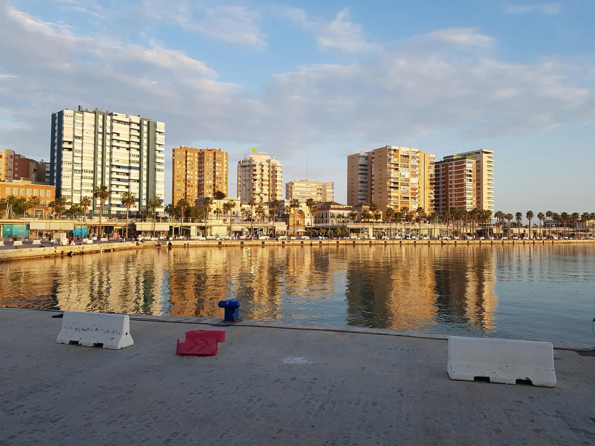 Edificios del paseo de la Farola reflejados en el agua del puerto de Málaga al atardecer