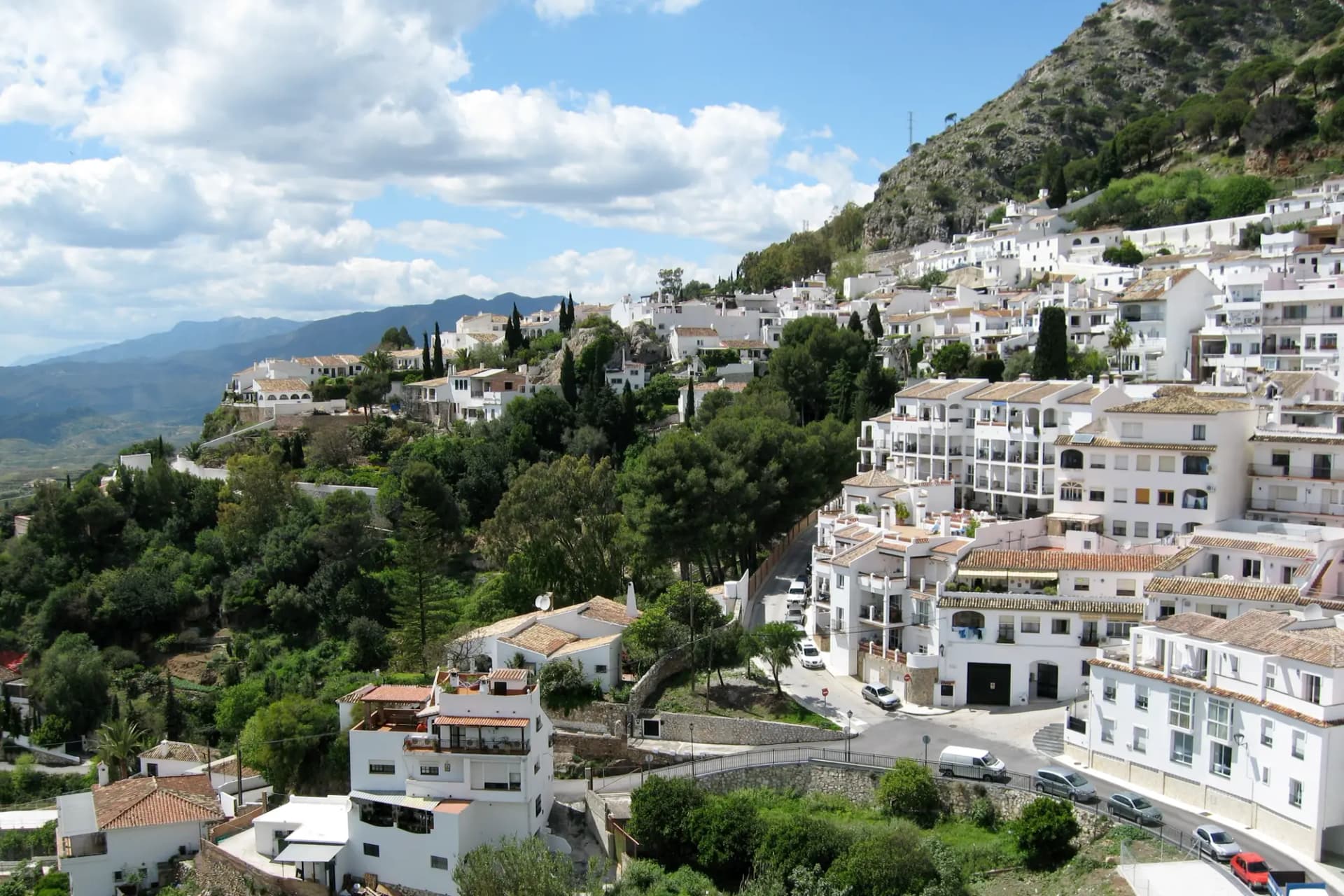 Casas blancas de Mijas Pueblo en la ladera de la sierra, entre vegetación, con la costa al fondo