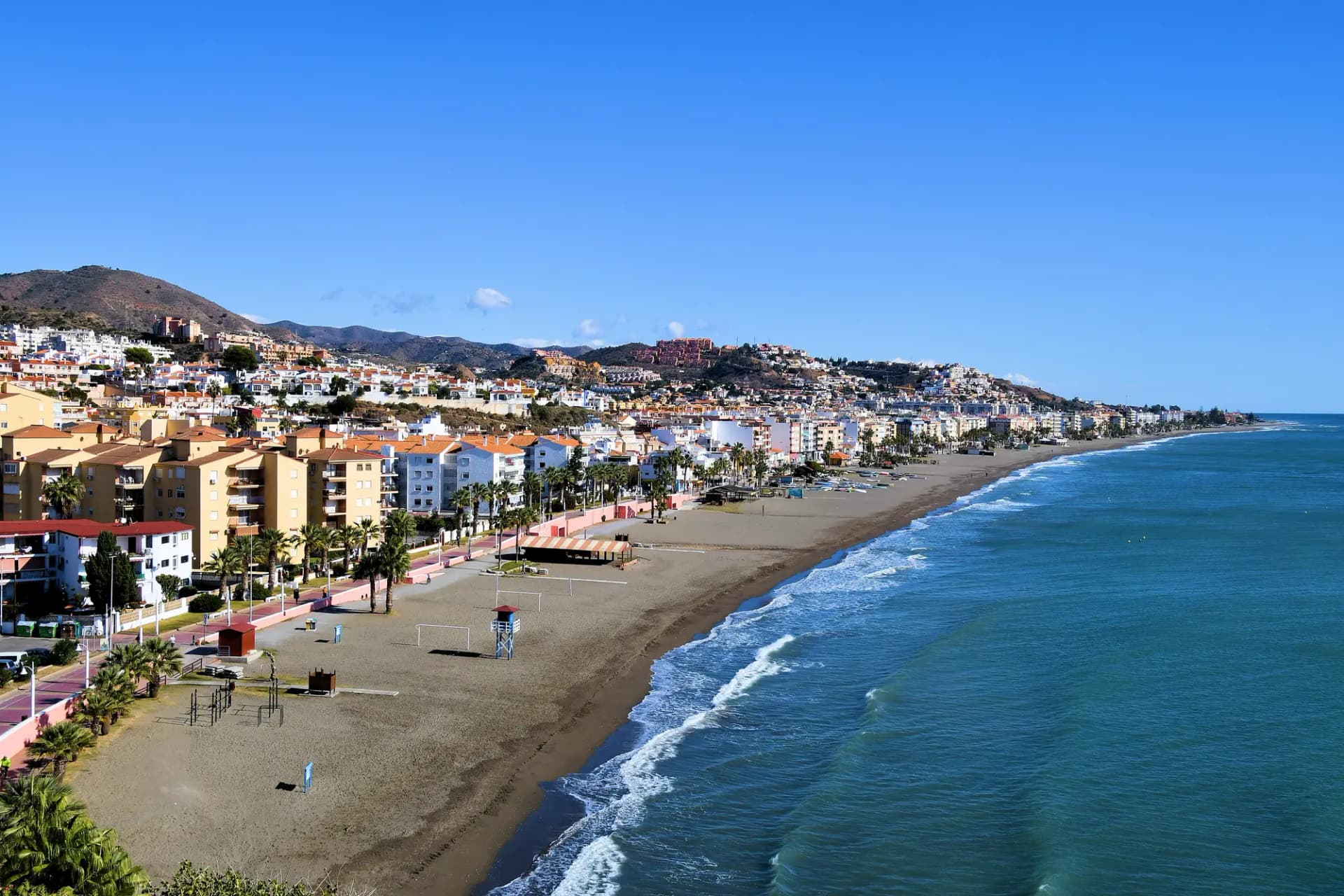 Playa y paseo marítimo de Rincón de la Victoria con bloques de viviendas y las lomas de los Montes de Málaga detrás