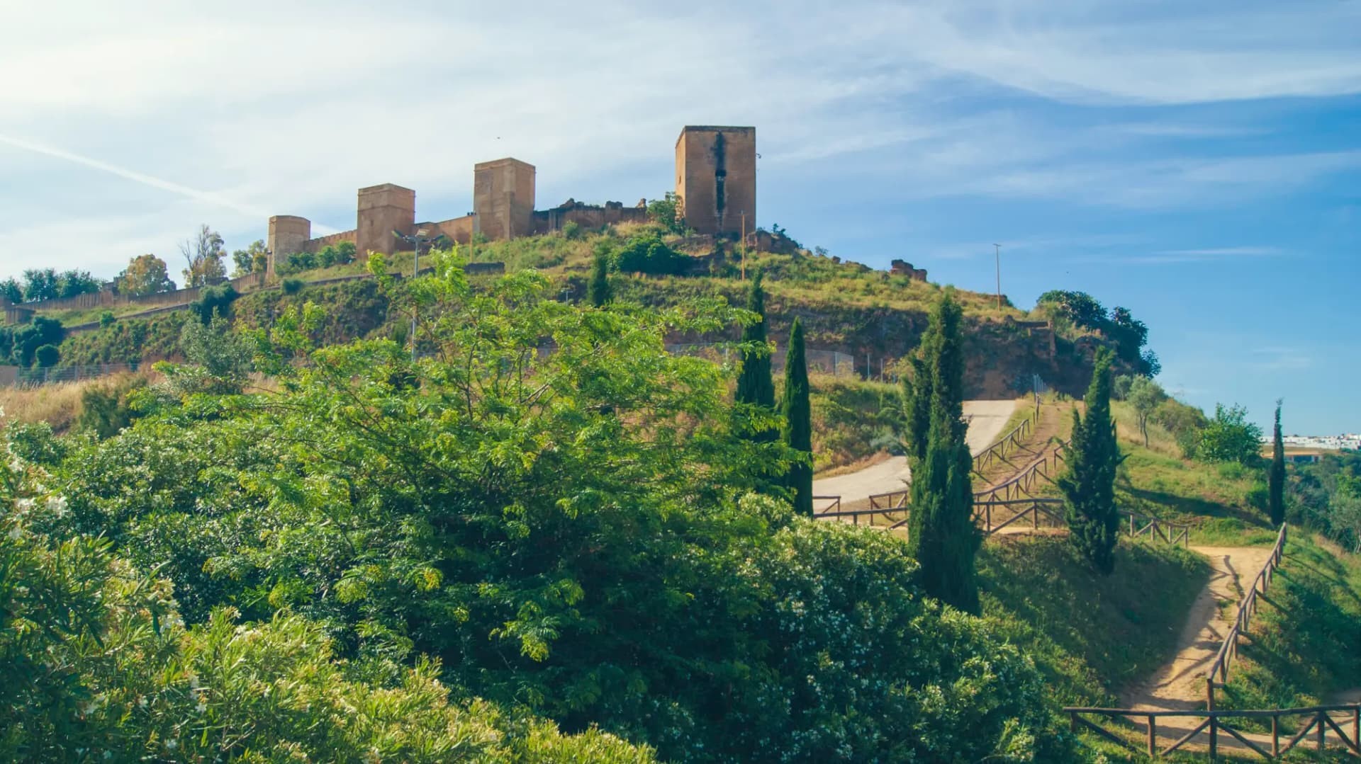 Torres y murallas del castillo de Alcalá de Guadaíra sobre un cerro cubierto de árboles y senderos