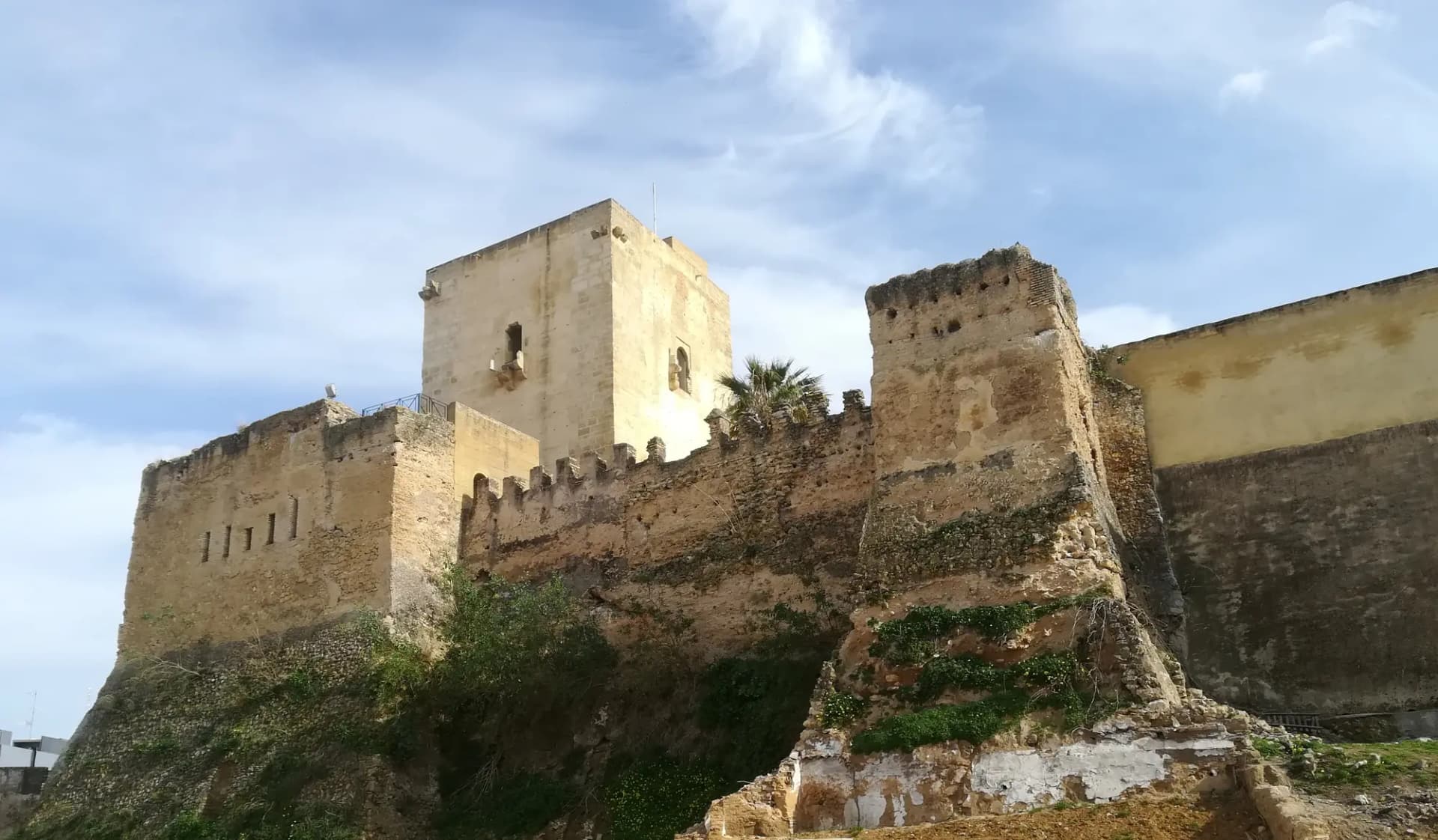 Torre del homenaje y murallas almenadas del castillo de Utrera bajo un cielo con nubes