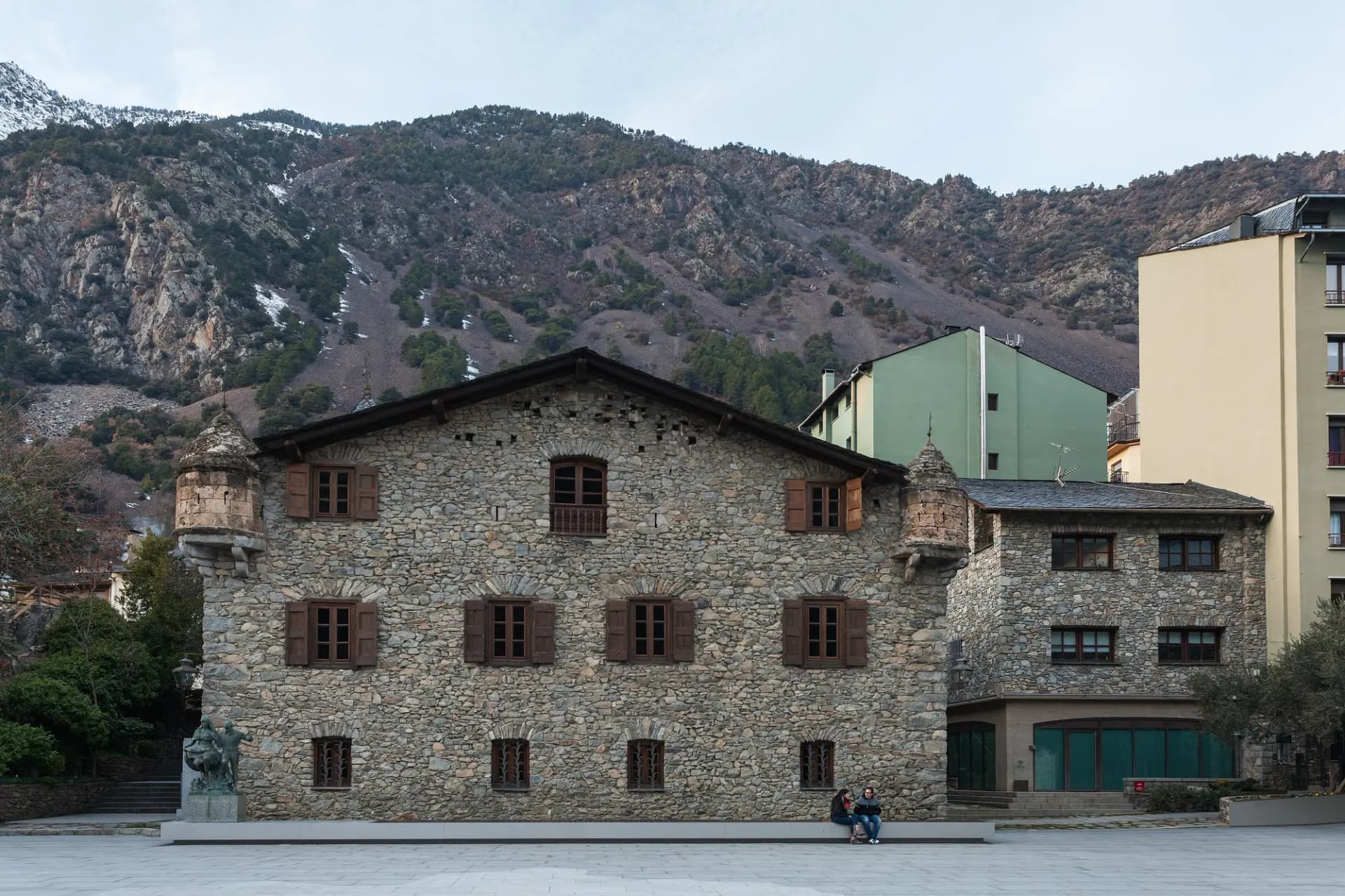 Fachada de piedra de la Casa de la Vall, con sus torretas en las esquinas y la montaña detrás