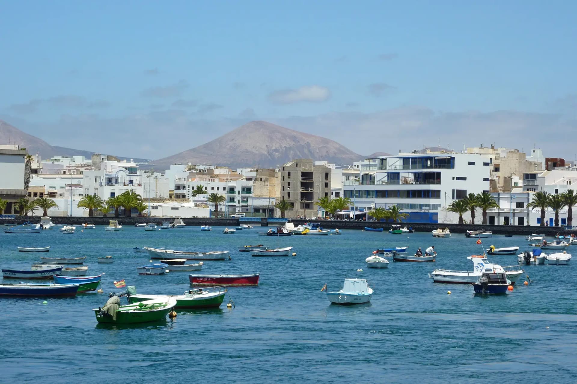 Barcas de pesca en el Charco de San Ginés, con casas blancas y una montaña volcánica al fondo