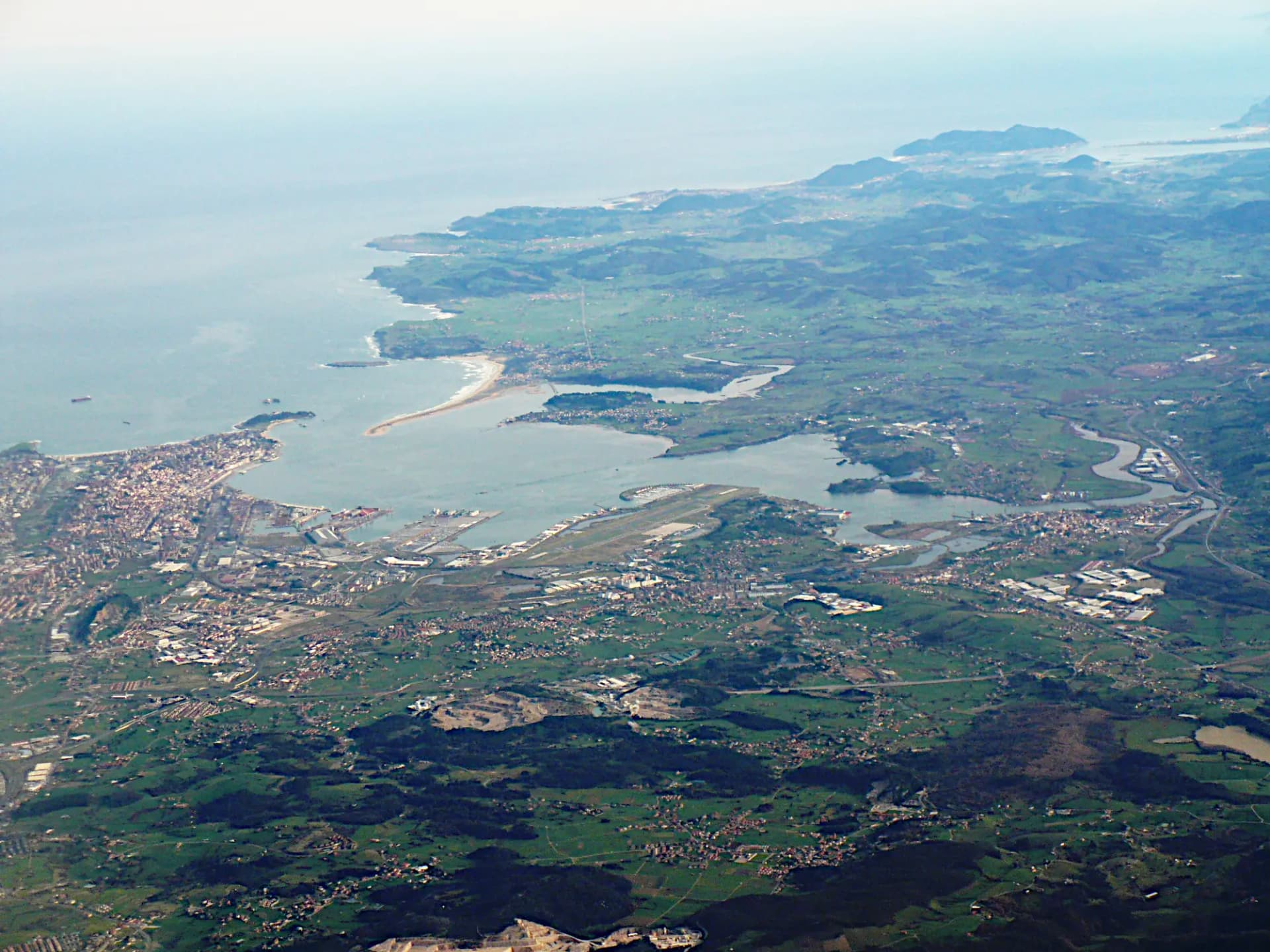 Vista aérea de la bahía de Santander, con la ciudad, el puerto, el aeropuerto y el arenal de El Puntal entre prados