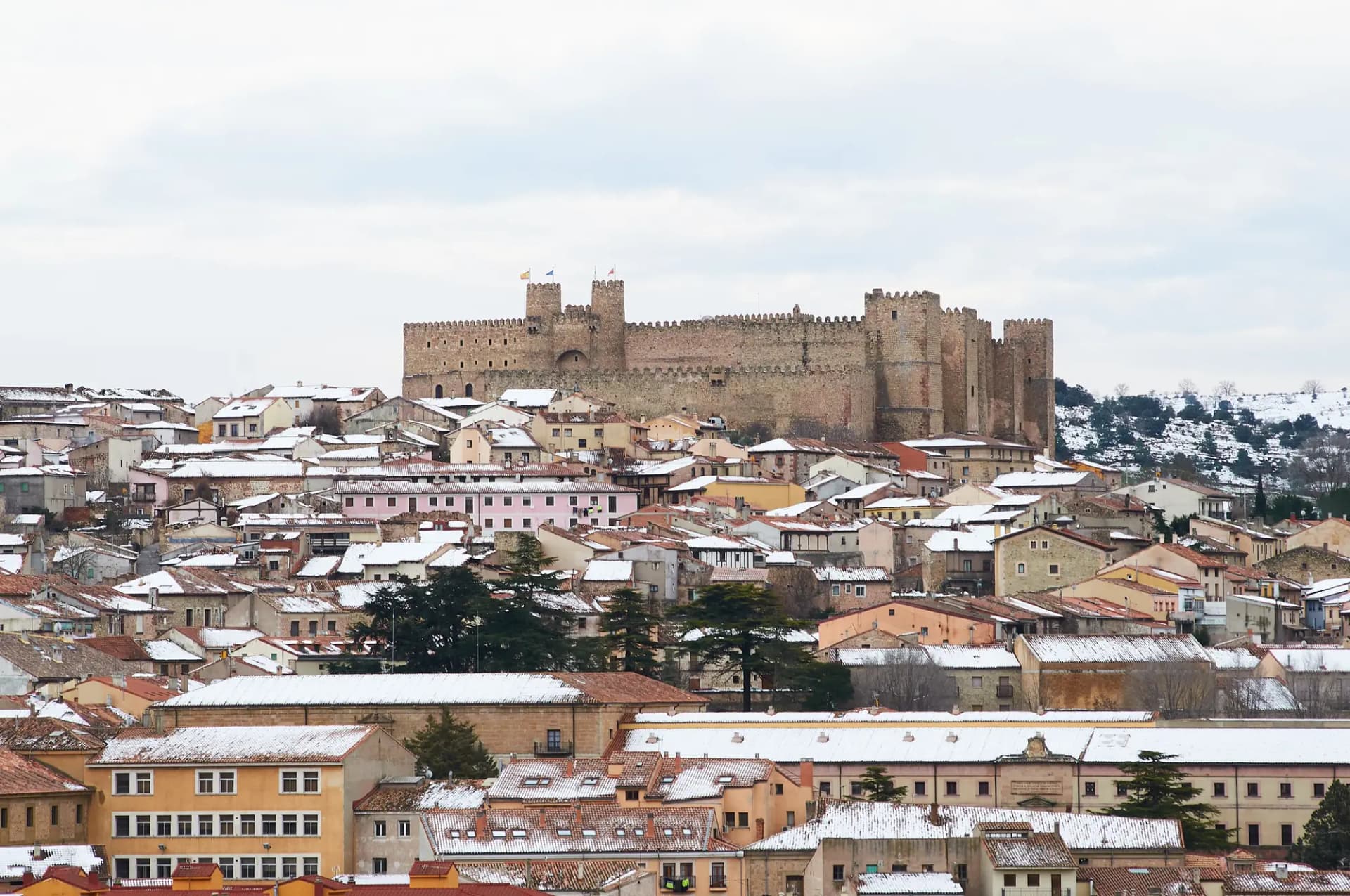 Castillo de Sigüenza sobre los tejados del casco antiguo, con nieve en las colinas