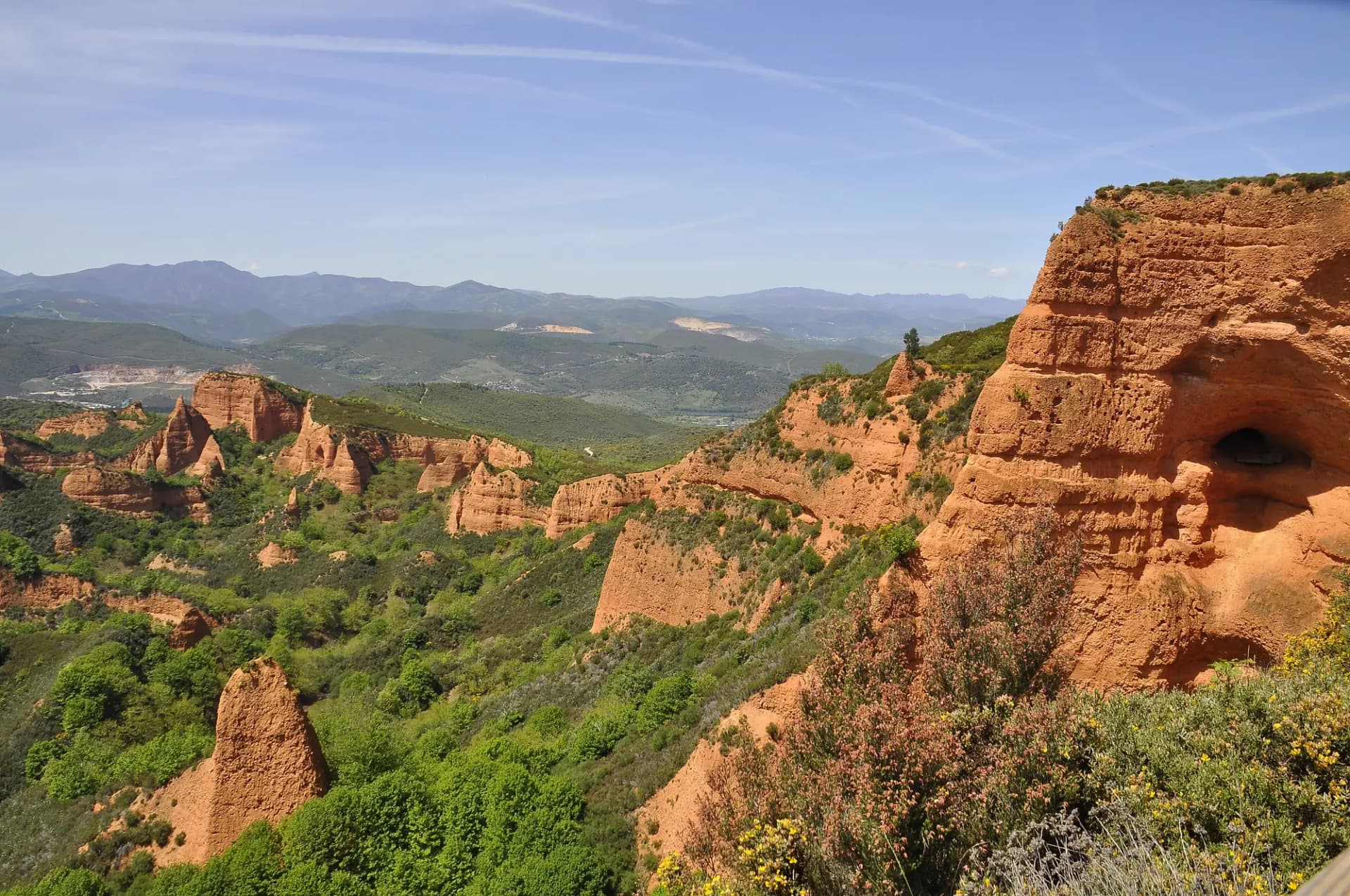 Picachos de arcilla rojiza de Las Médulas entre castaños, con montañas al fondo