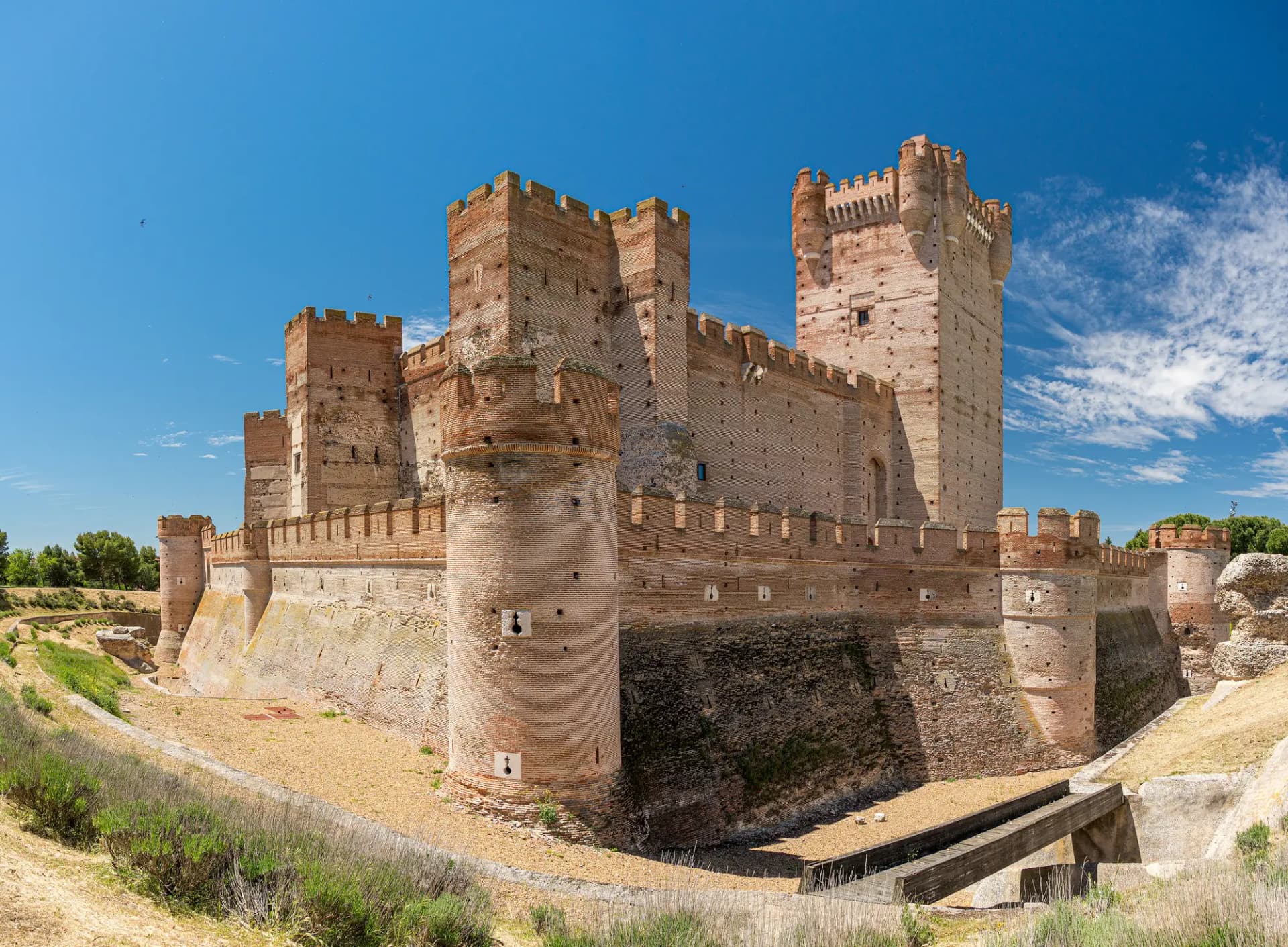 Castillo de ladrillo de la Mota, con su torre del homenaje y la muralla sobre el foso, bajo un cielo azul