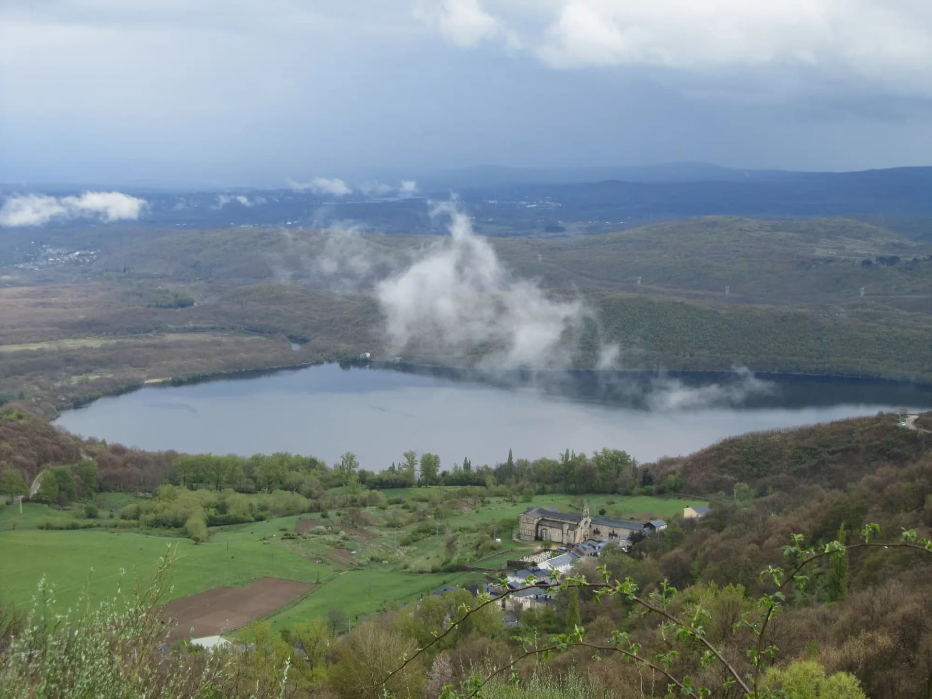 Lago de Sanabria entre montes con nubes bajas y el pueblo de San Martín de Castañeda en primer plano