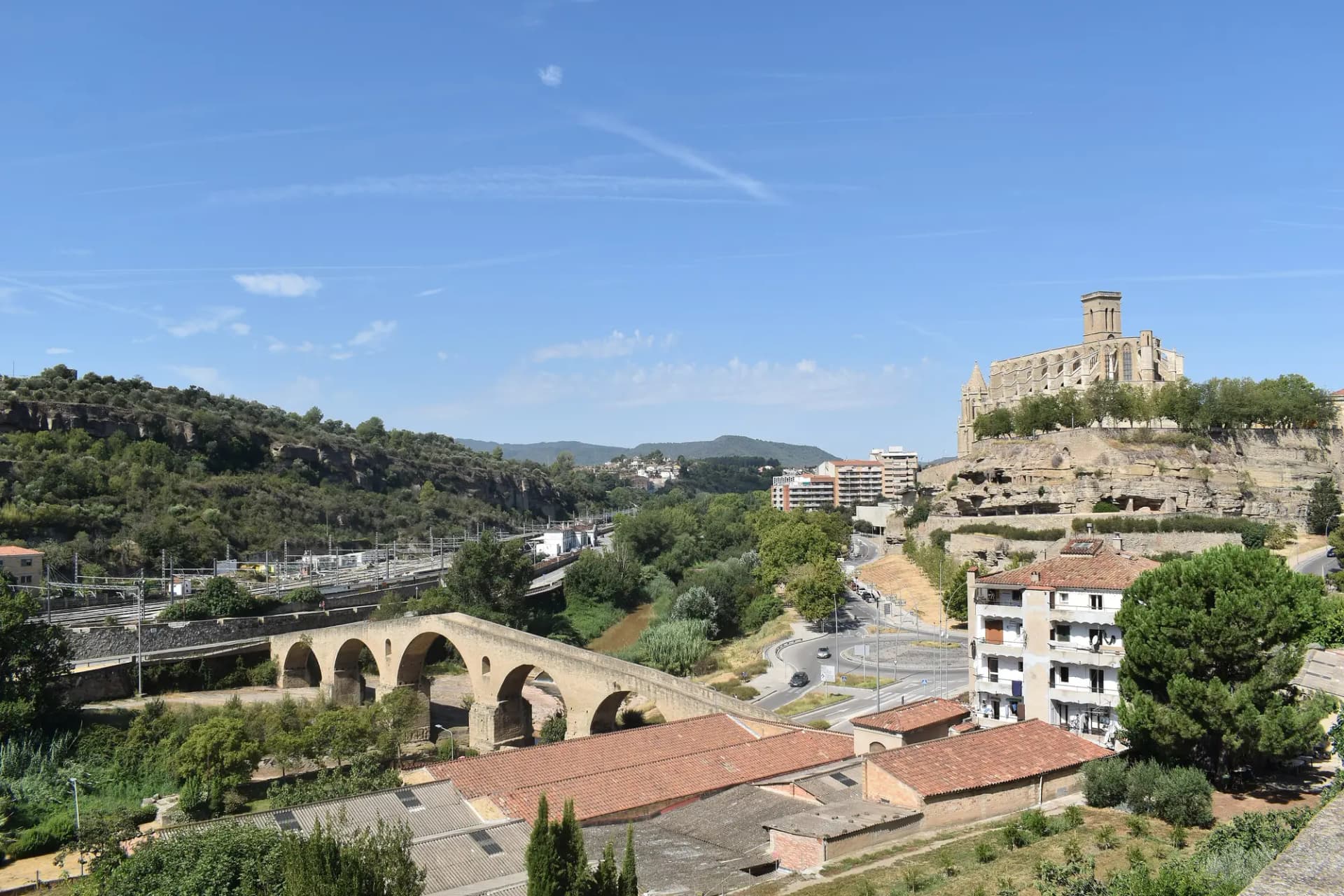 Vista de Manresa con el Pont Vell sobre el Cardener y la basílica de la Seu en lo alto de la roca, bajo un cielo azul