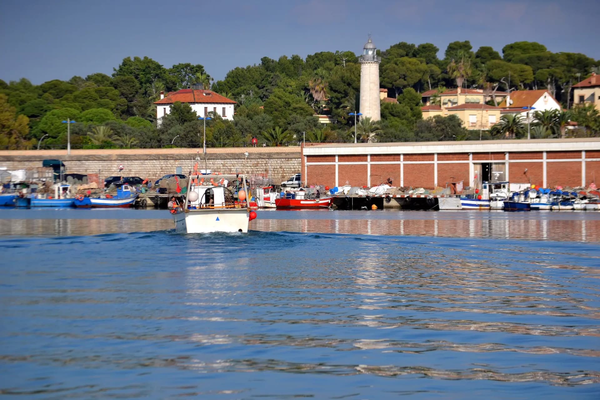 Barca de pesca entrando en el puerto de Vilanova i la Geltrú con el faro de Sant Cristòfol al fondo