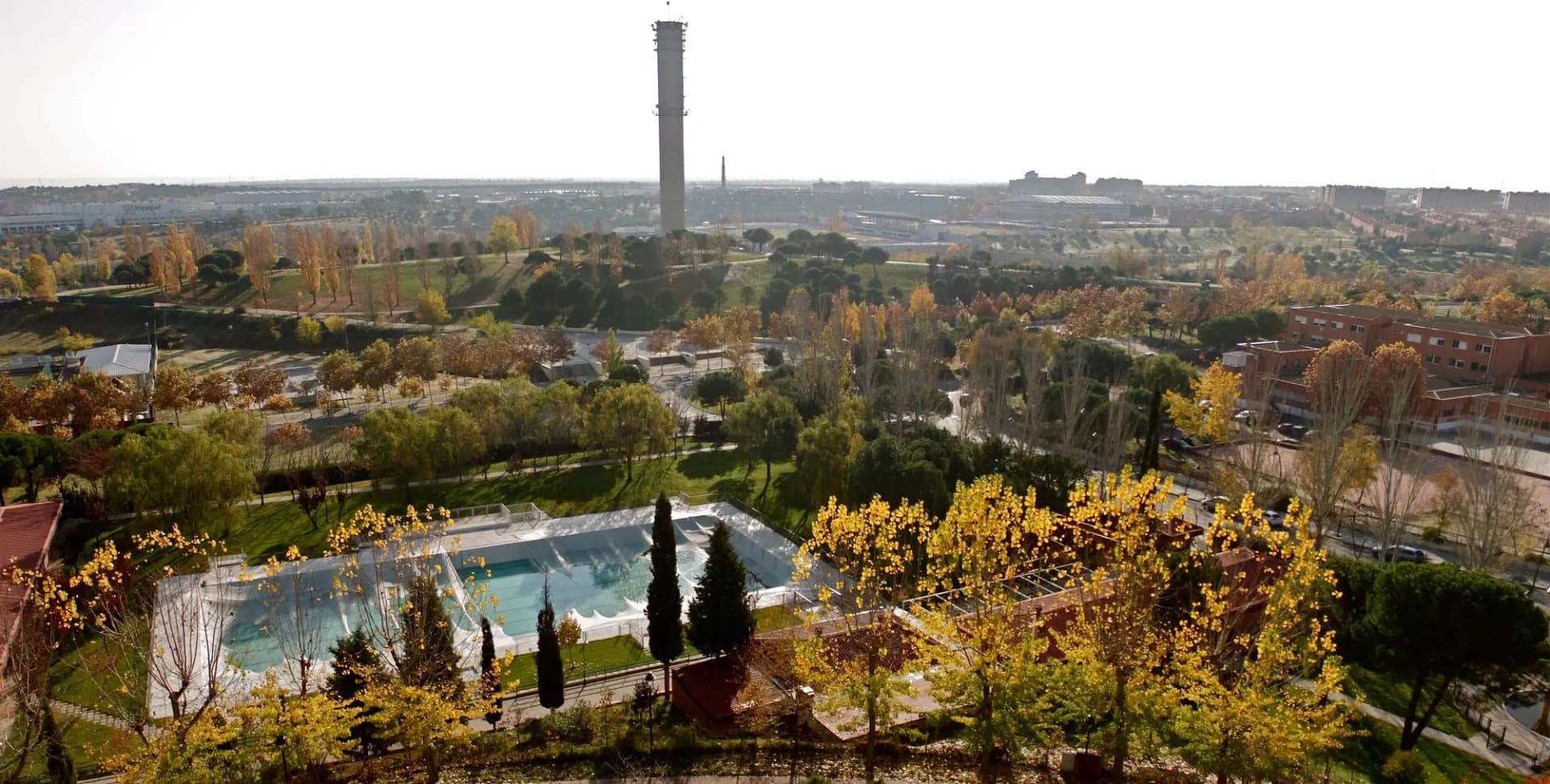 Vista de Tres Cantos desde lo alto, con parques arbolados en otoño, una piscina y una torre al fondo