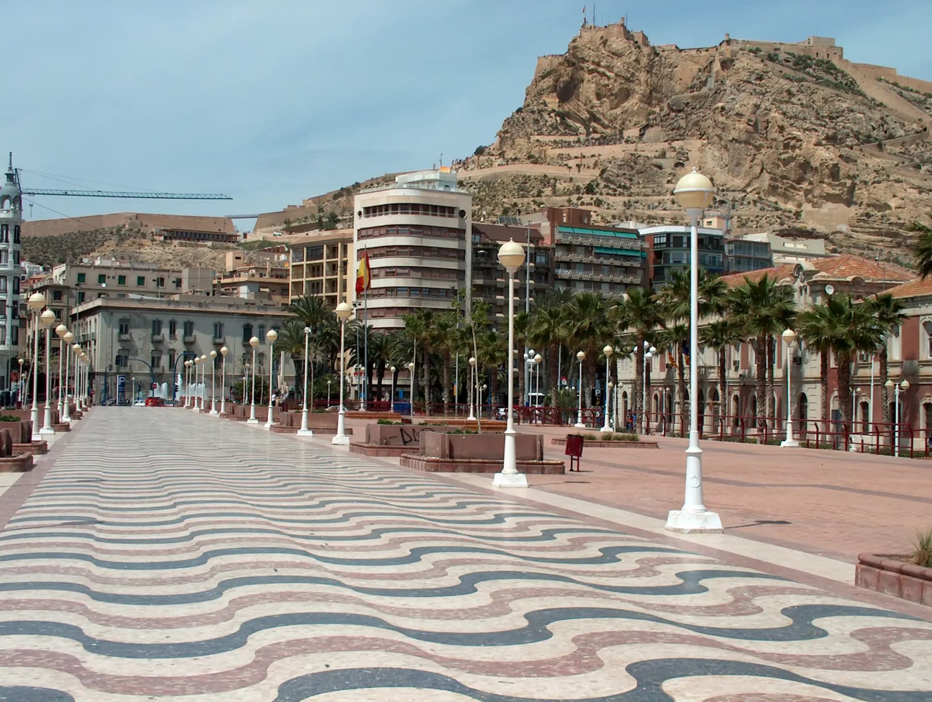 Paseo de la Explanada de Alicante con su suelo de mosaico ondulado, palmeras y el castillo de Santa Bárbara al fondo