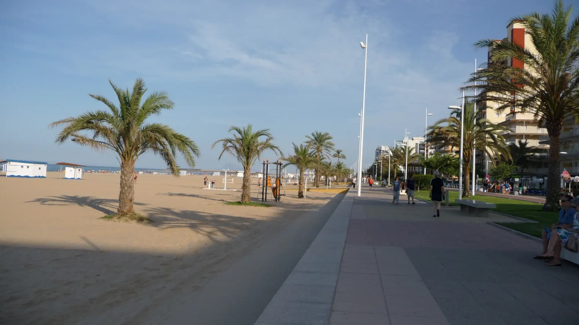 Paseo marítimo de la playa de Gandia con palmeras, la arena a la izquierda y edificios de apartamentos al fondo