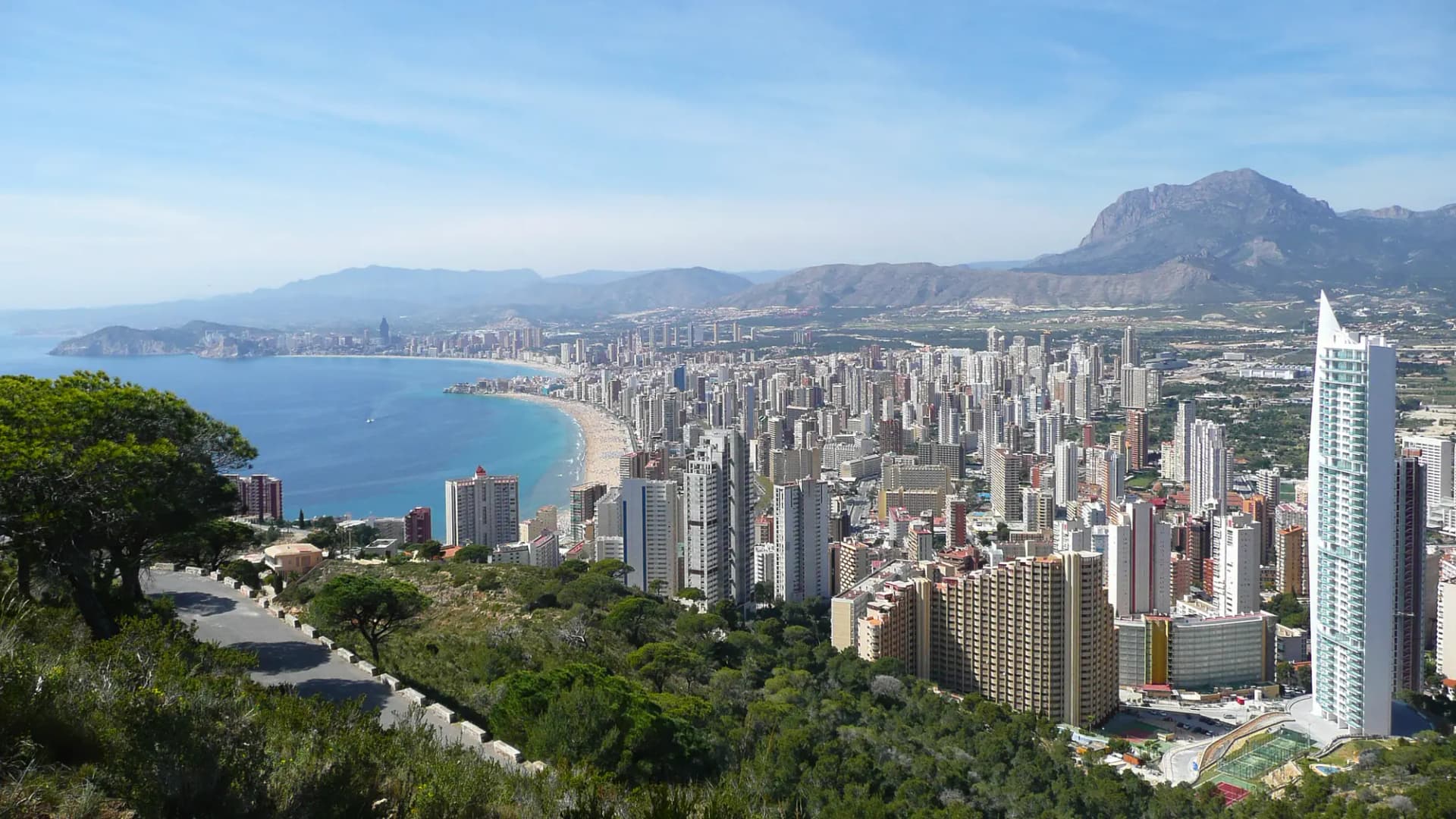 Vista elevada de Benidorm con su bahía, la playa y los rascacielos, y las montañas detrás