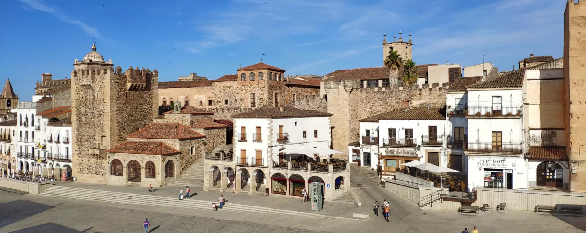 Plaza Mayor de Cáceres con la muralla, la Torre de Bujaco y casas blancas con soportales al sol