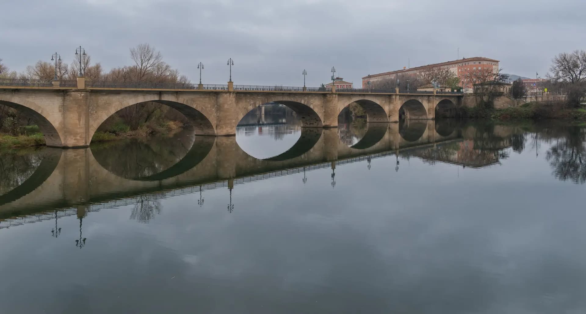 El Puente de Piedra de Logroño sobre el río Ebro, con sus arcos reflejados en el agua en un día nublado