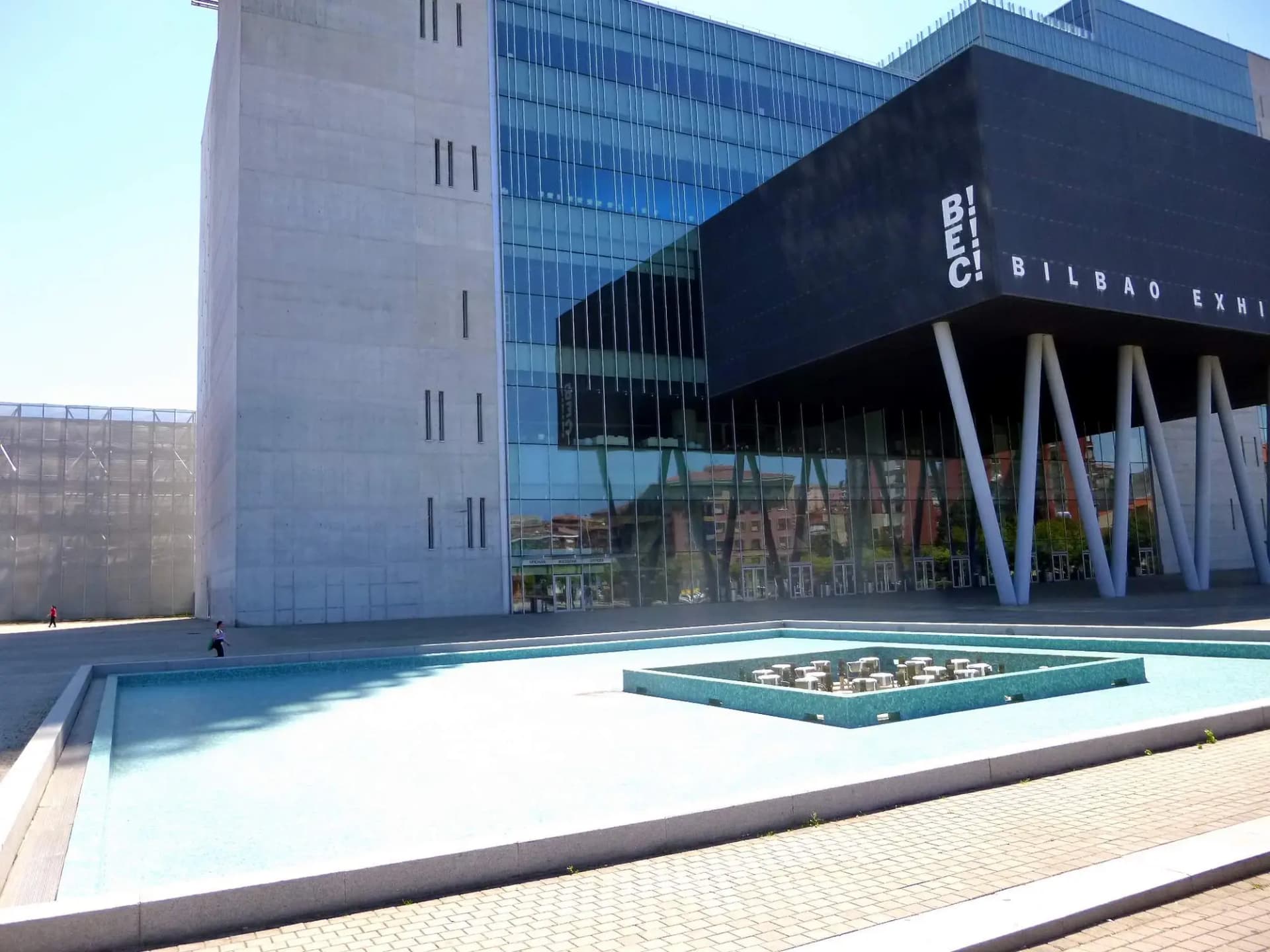 Entrada del Bilbao Exhibition Centre en Barakaldo, con su torre de oficinas, la fachada de cristal y la lámina de agua delante