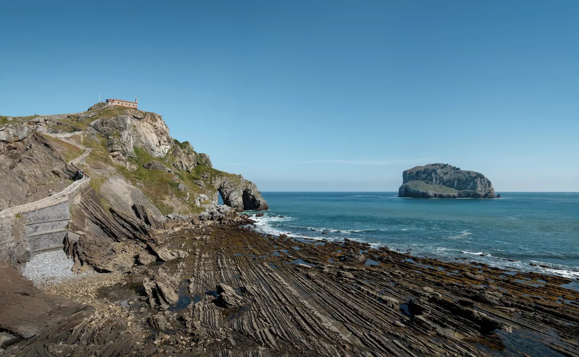Peñón de San Juan de Gaztelugatxe con la ermita en lo alto, la escalera de piedra y el islote de Aketx en el mar