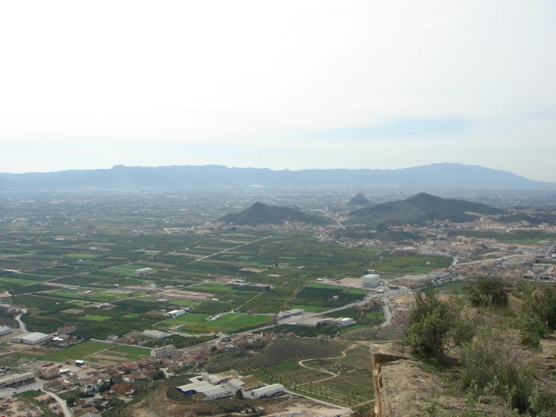 Vista desde lo alto de la huerta de Murcia, con parcelas de cultivo, naves y sierras al fondo
