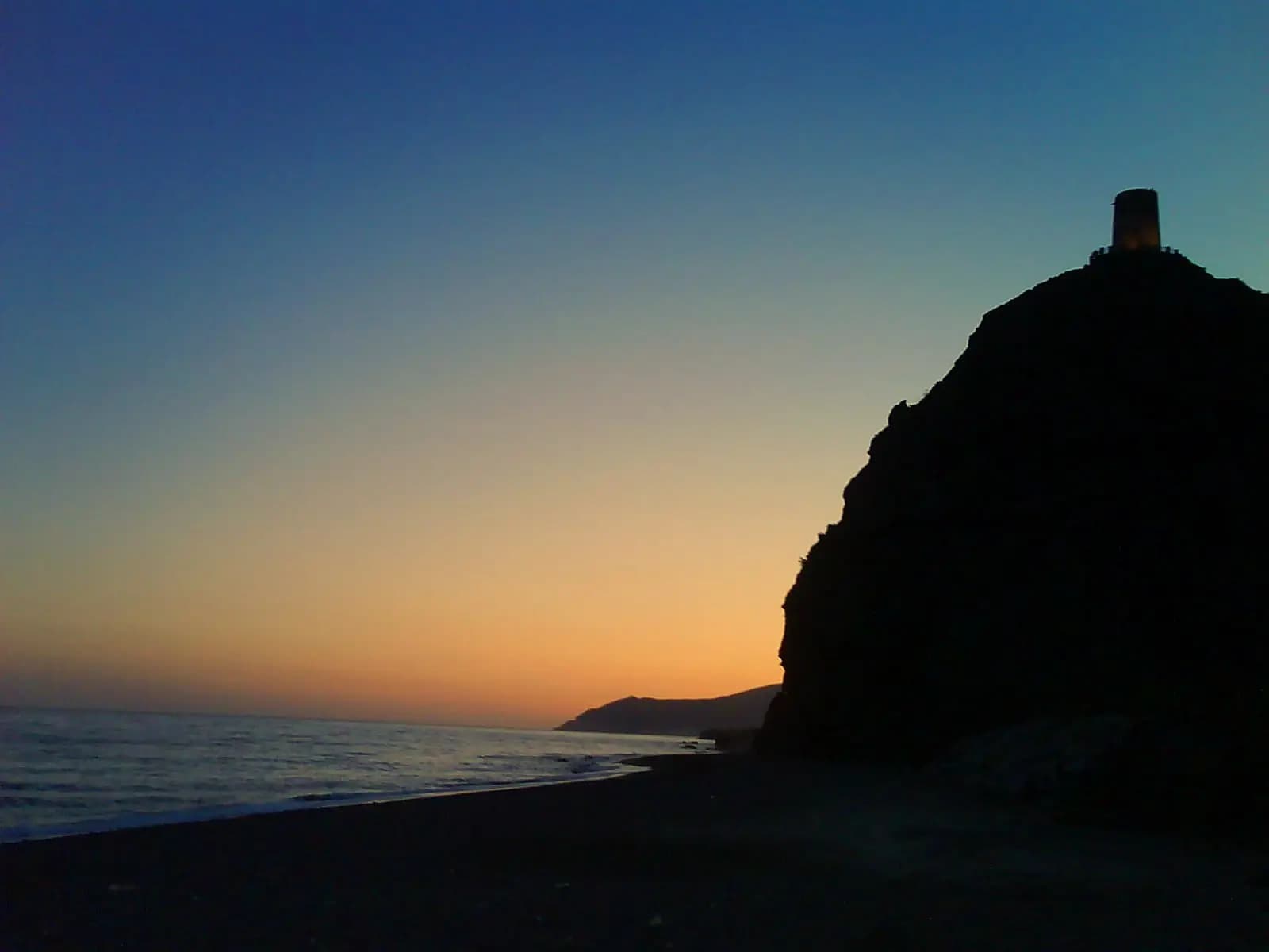 Playa de La Mamola al atardecer con la Torre del Cautor sobre el cerro