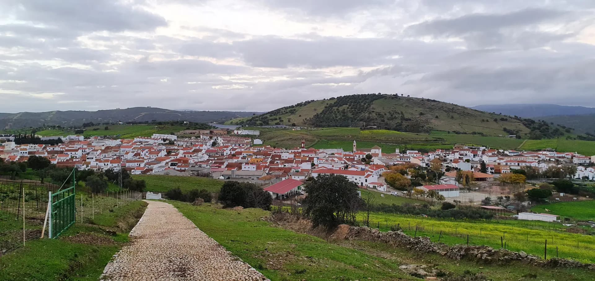 Vista de Almadén de la Plata desde un camino, con el pueblo en el valle y los montes de Sierra Morena detrás