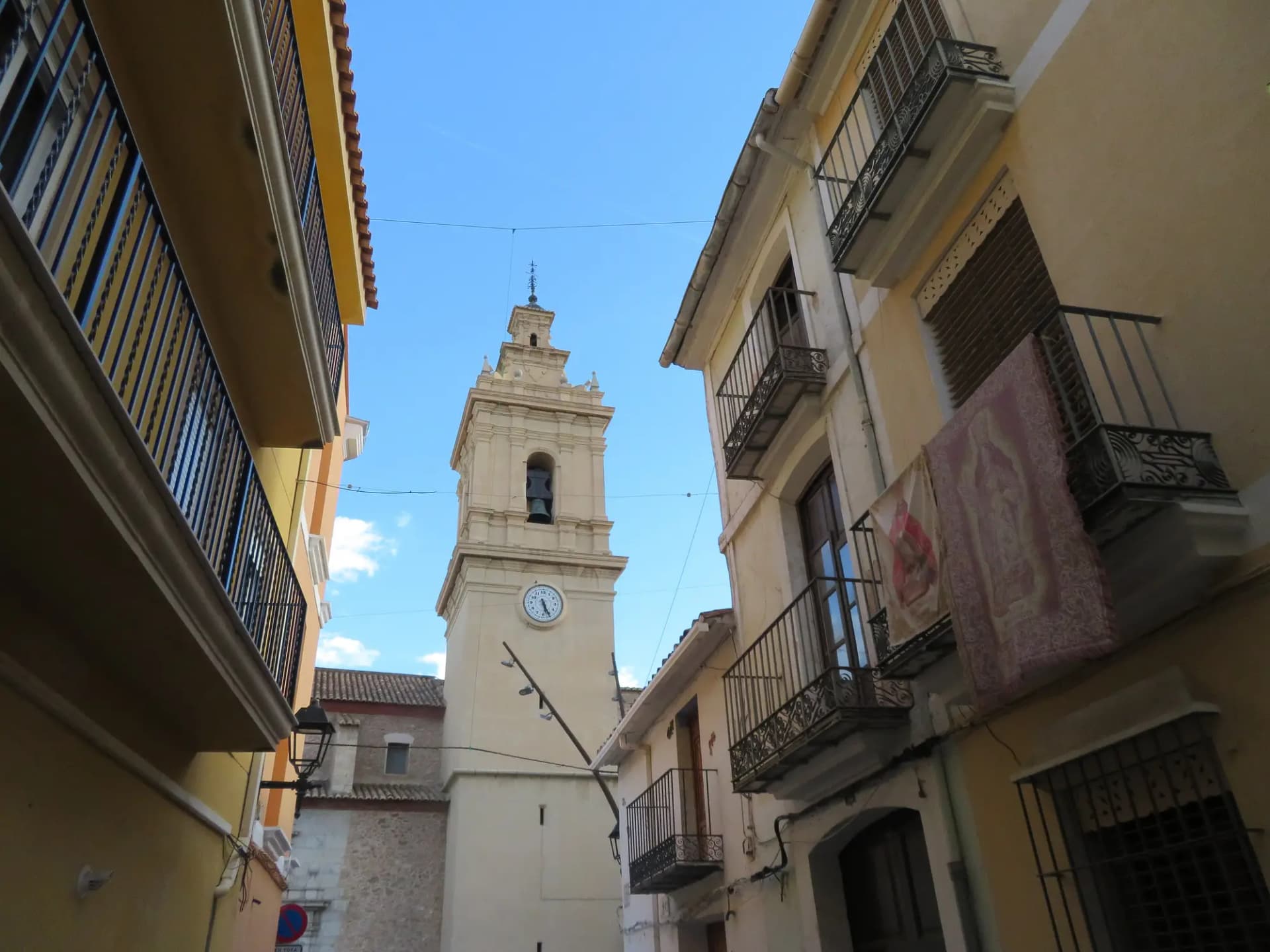 Campanario de la iglesia de la Natividad de Almassora visto desde una calle del centro con balcones