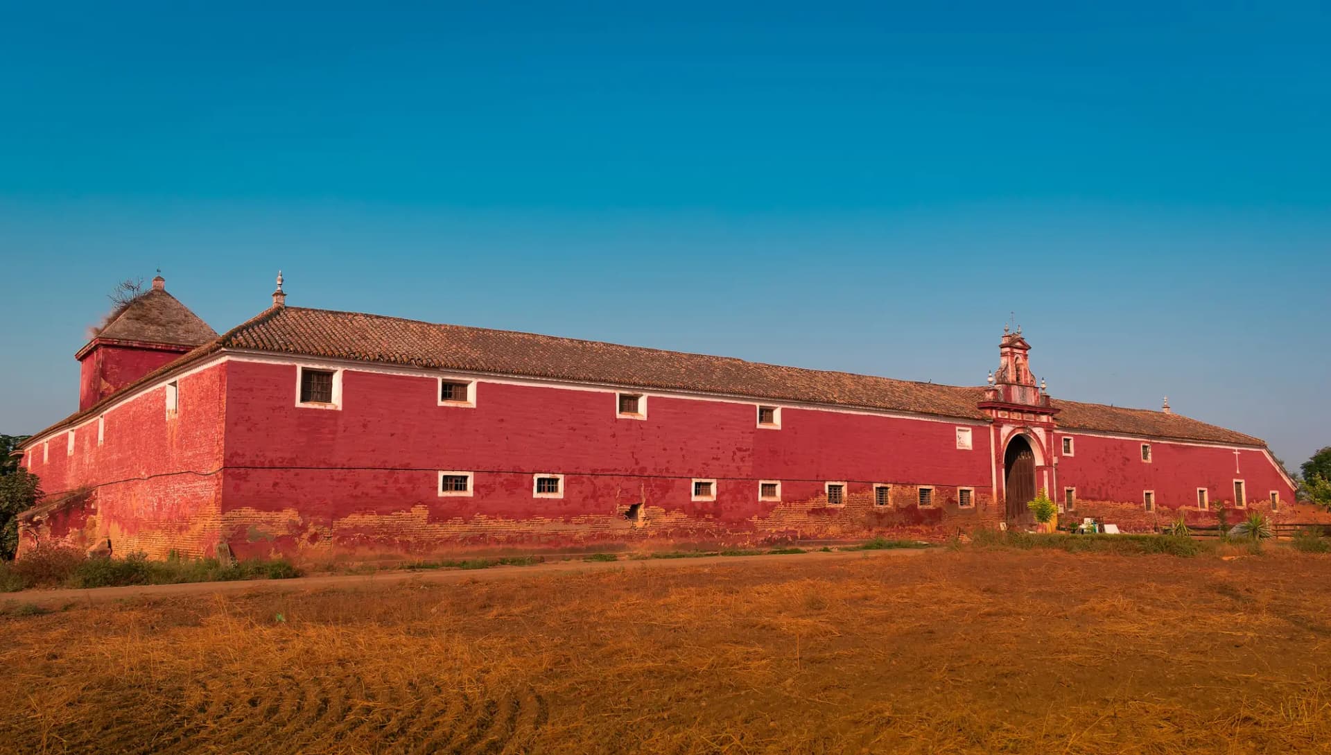 Caserío alargado de muros rojizos y espadaña de la hacienda de Ibarburu, sobre un campo seco