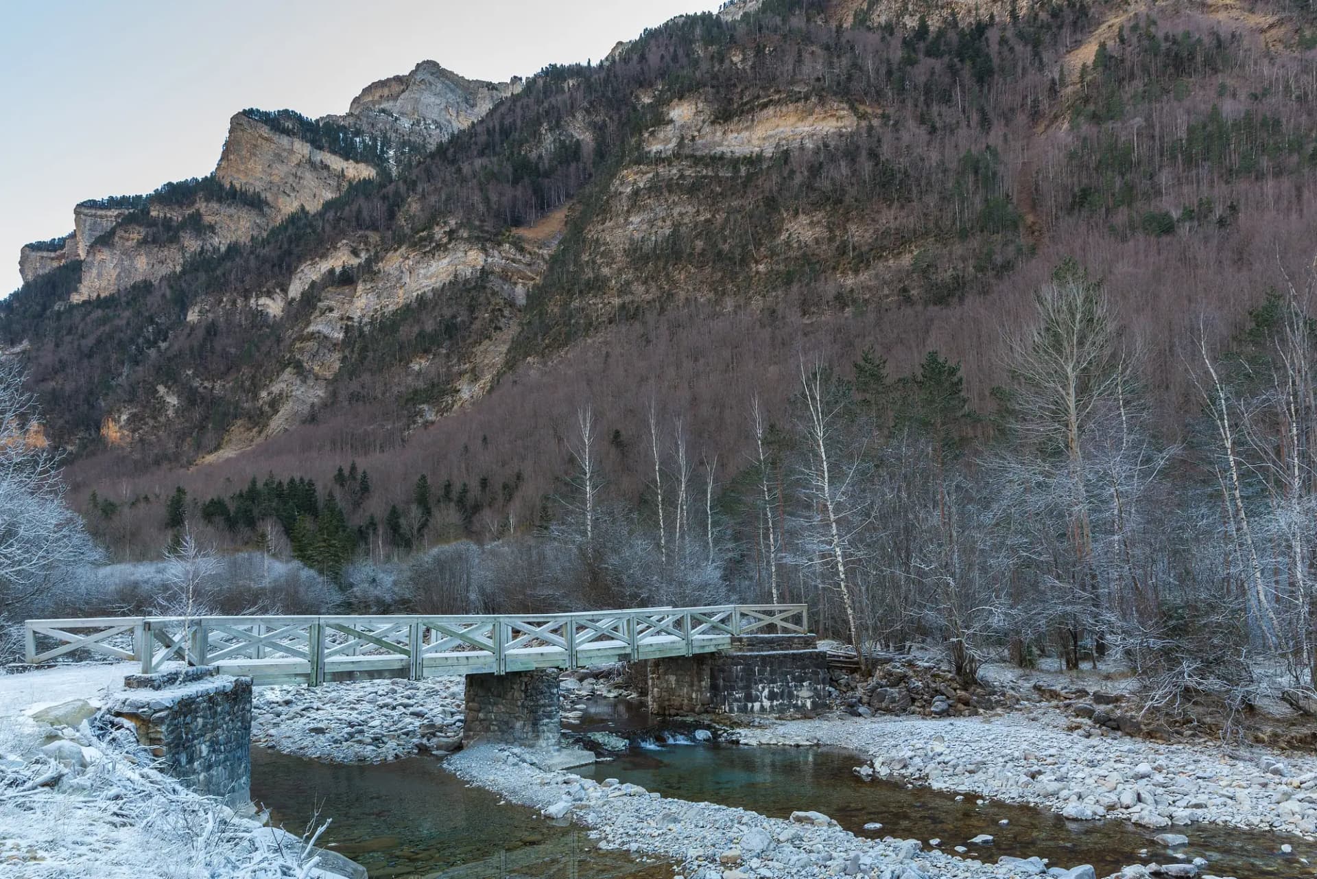 Valle de Ordesa en invierno, con un puente sobre el río, orillas escarchadas y paredes de roca al fondo